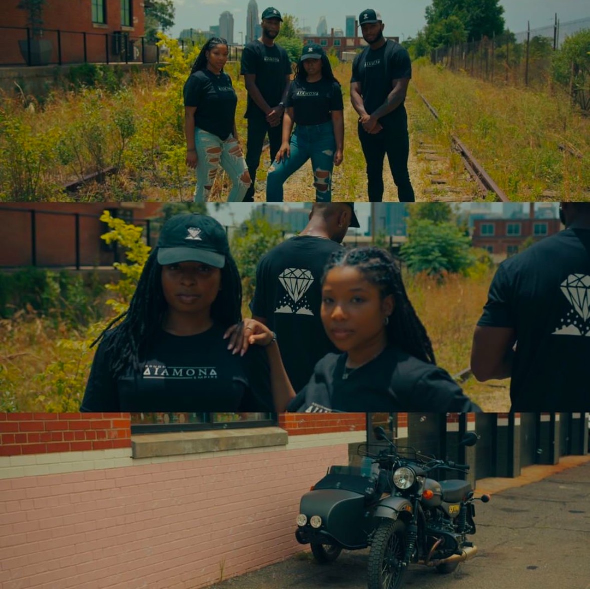 Group of five people standing on train tracks outdoors, two women in front, one wearing a cap, motorcycle parked nearby, sunny day.