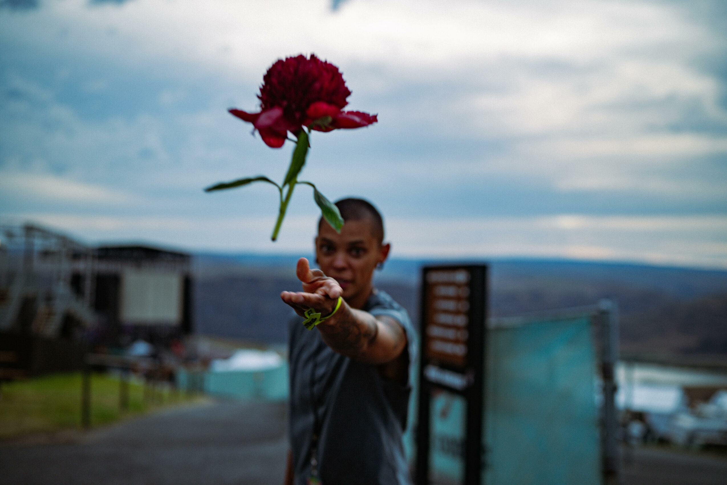 Child holding a flower with a cloudy sky background, pointing towards the camera.