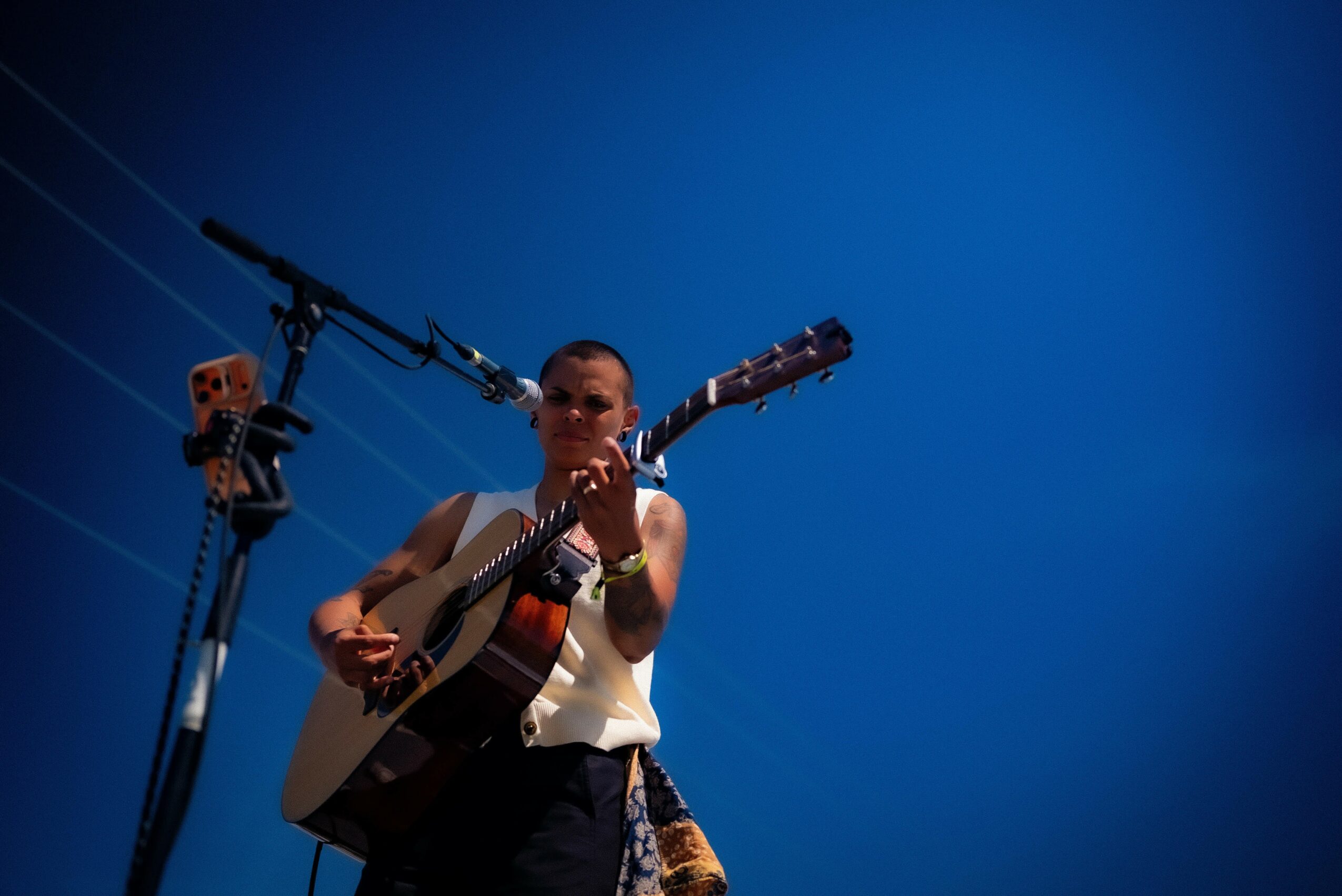 Person playing guitar on stage with a large camera mounted above, against a blue background.