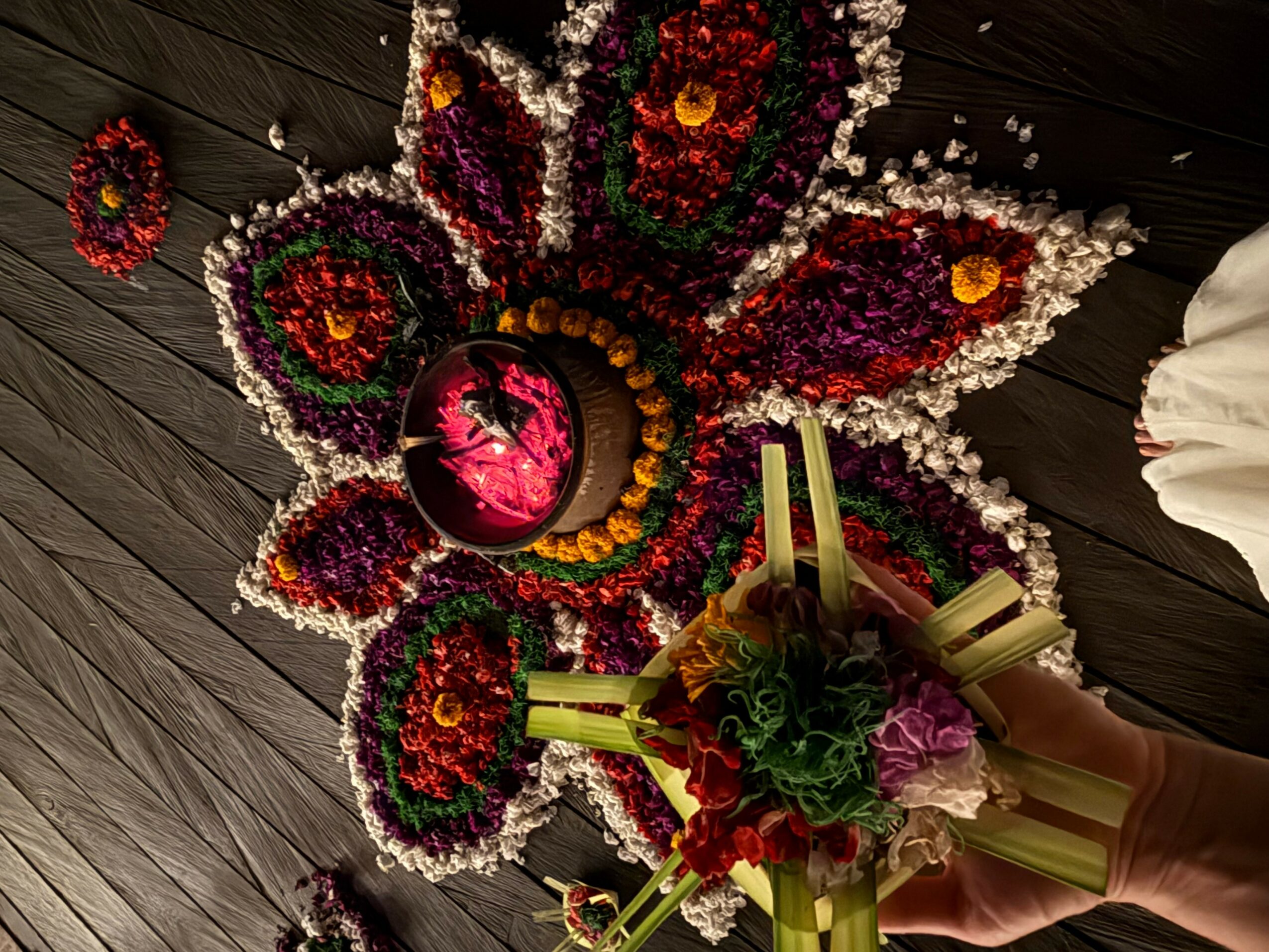 Person holding a bouquet of flowers near a butterfly-shaped floral arrangement on a wooden floor.