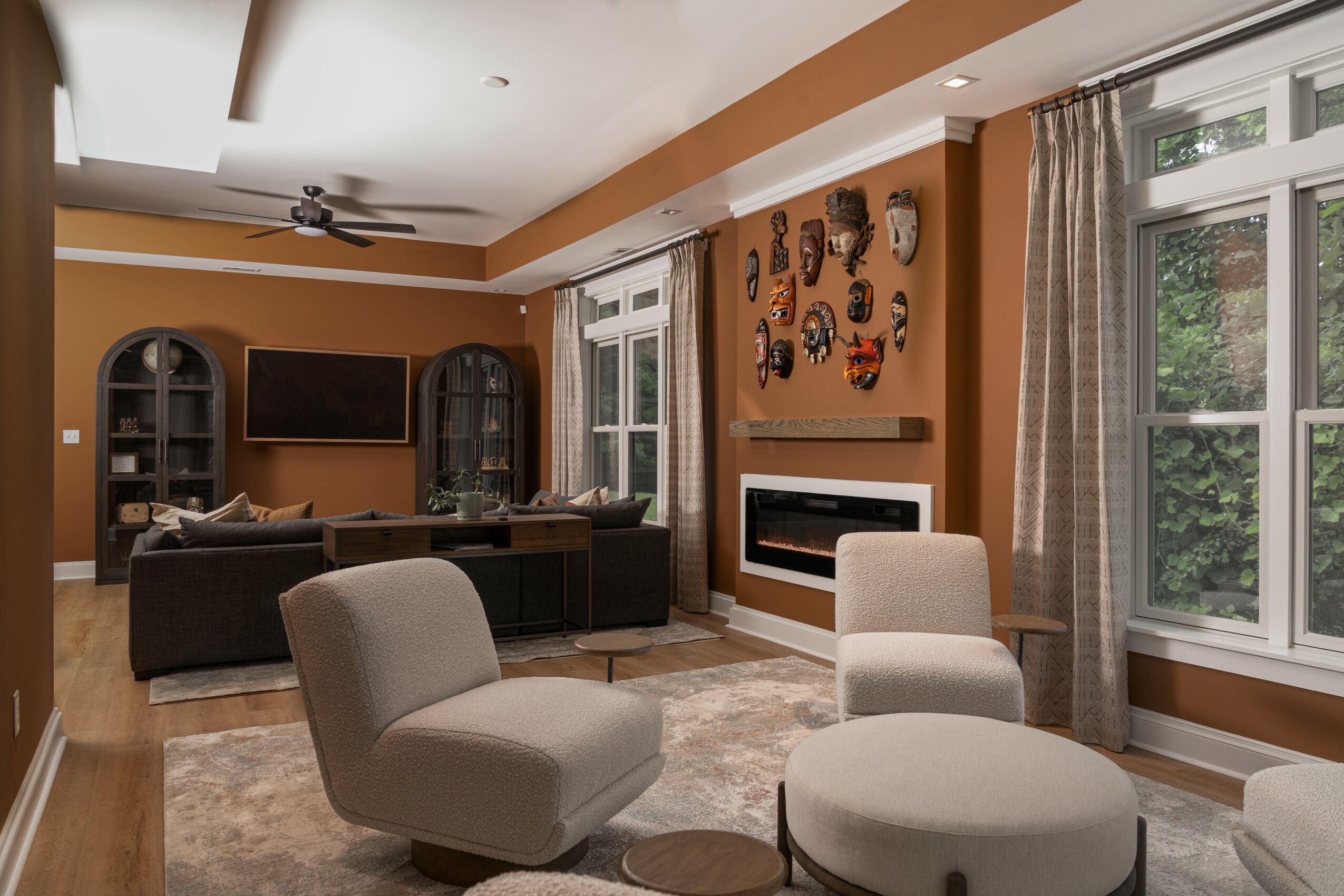 Living room with brown walls, large windows, beige curtains, and modern furniture including chairs, a sofa, and a fireplace.