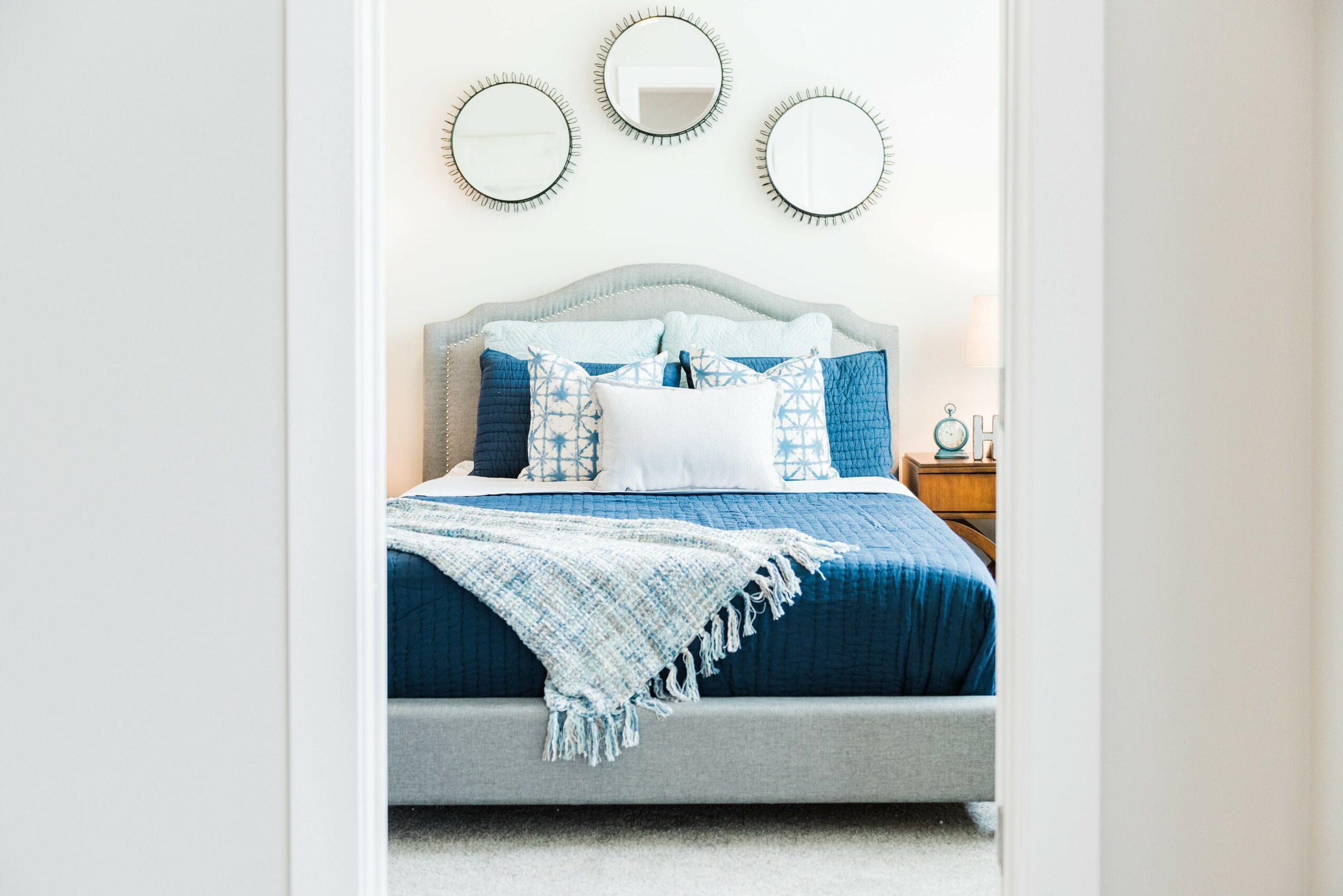 Bedroom with a bed, pillows, and a blanket, three round mirrors on the wall, and a nightstand with a lamp.