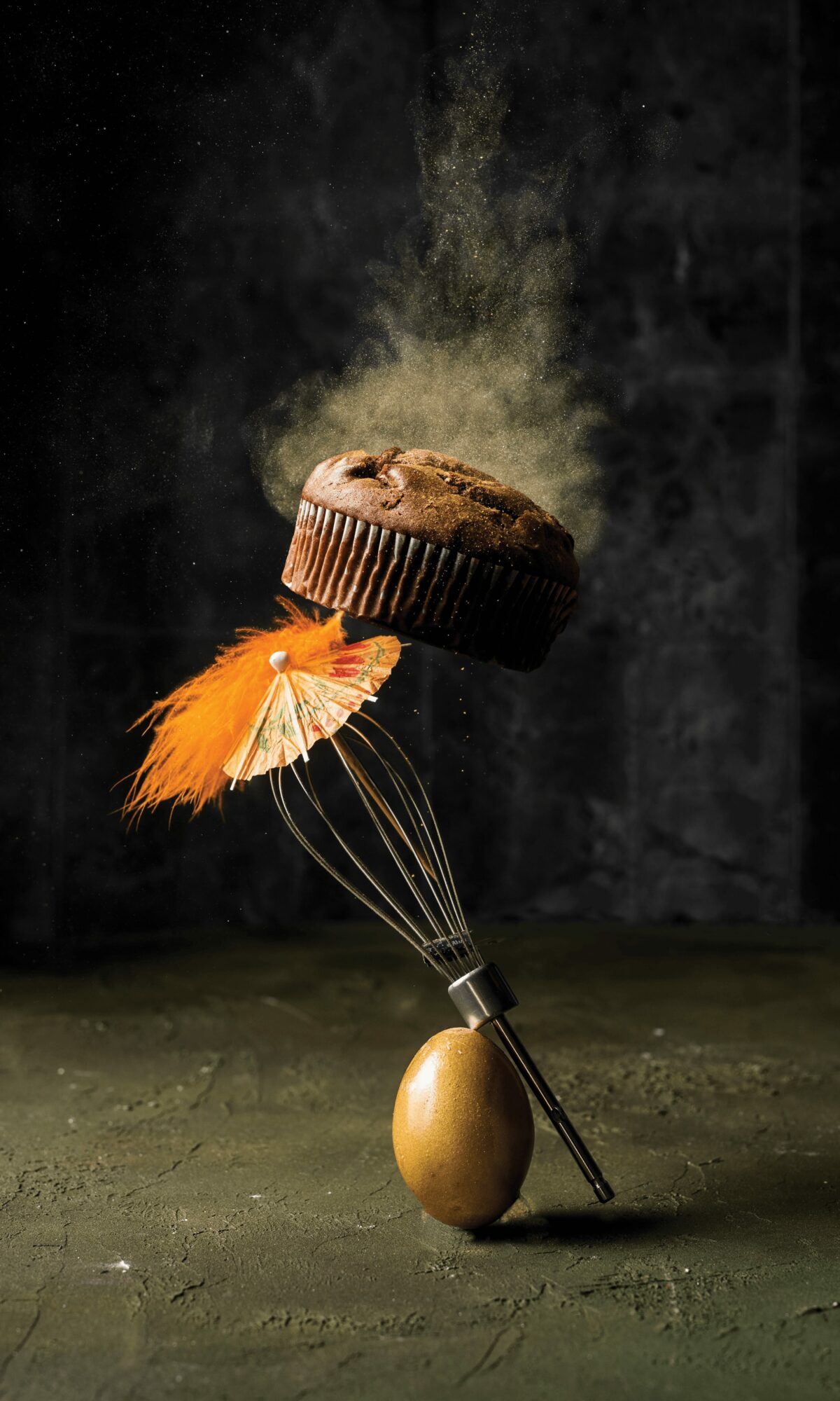 A cupcake with steam rising, balanced on a spoon, which is supported by an egg on a dark surface.