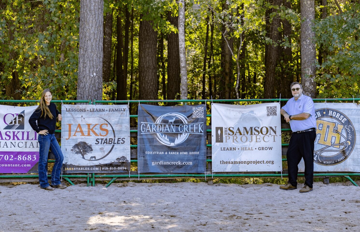 Two people standing outdoors in front of banners with trees in the background.