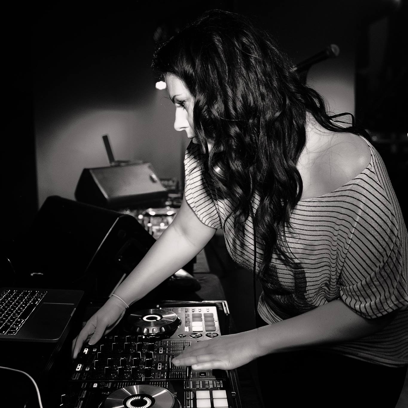 Woman with long dark hair operating DJ equipment in a dimly lit setting.