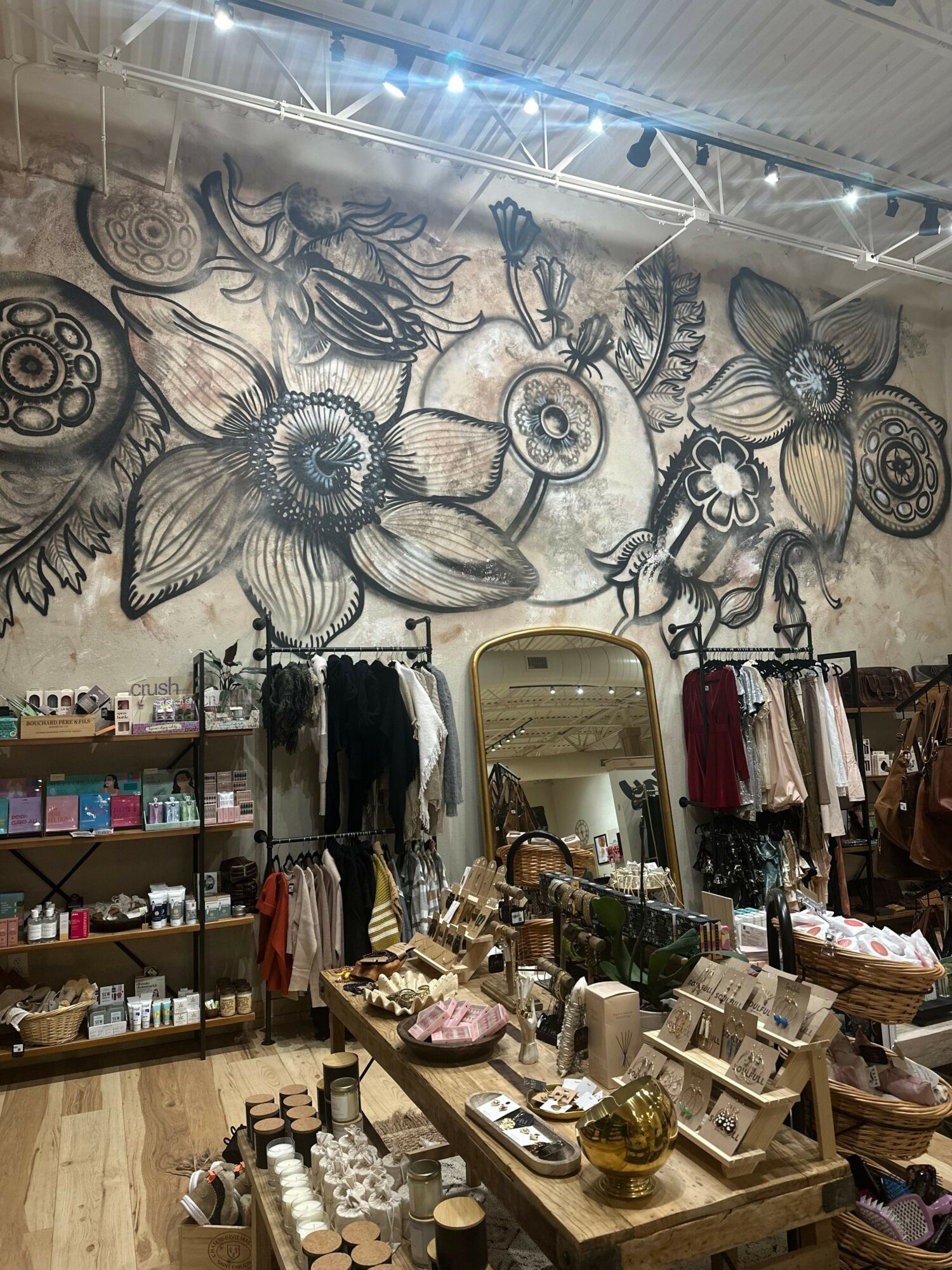 Store interior with shelves of cosmetics, accessories, and a mirror, viewed from the side. Various products are displayed on tables.