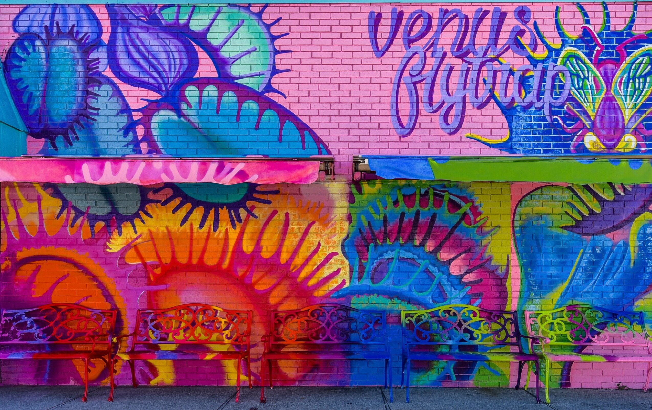 Colorful mural with abstract shapes, text, and benches in front, vibrant pink, purple, orange, blue, and green colors.