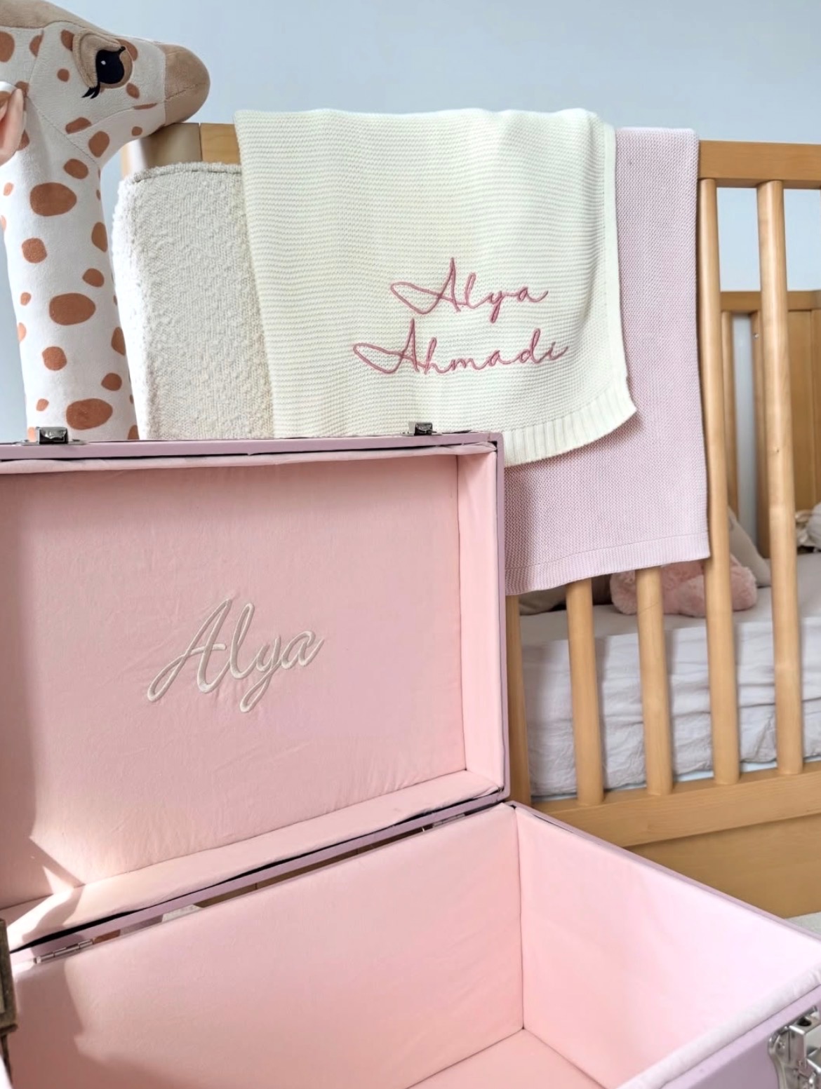 Baby crib with pink box, towels, and a stuffed animal in the background, against a light blue wall.