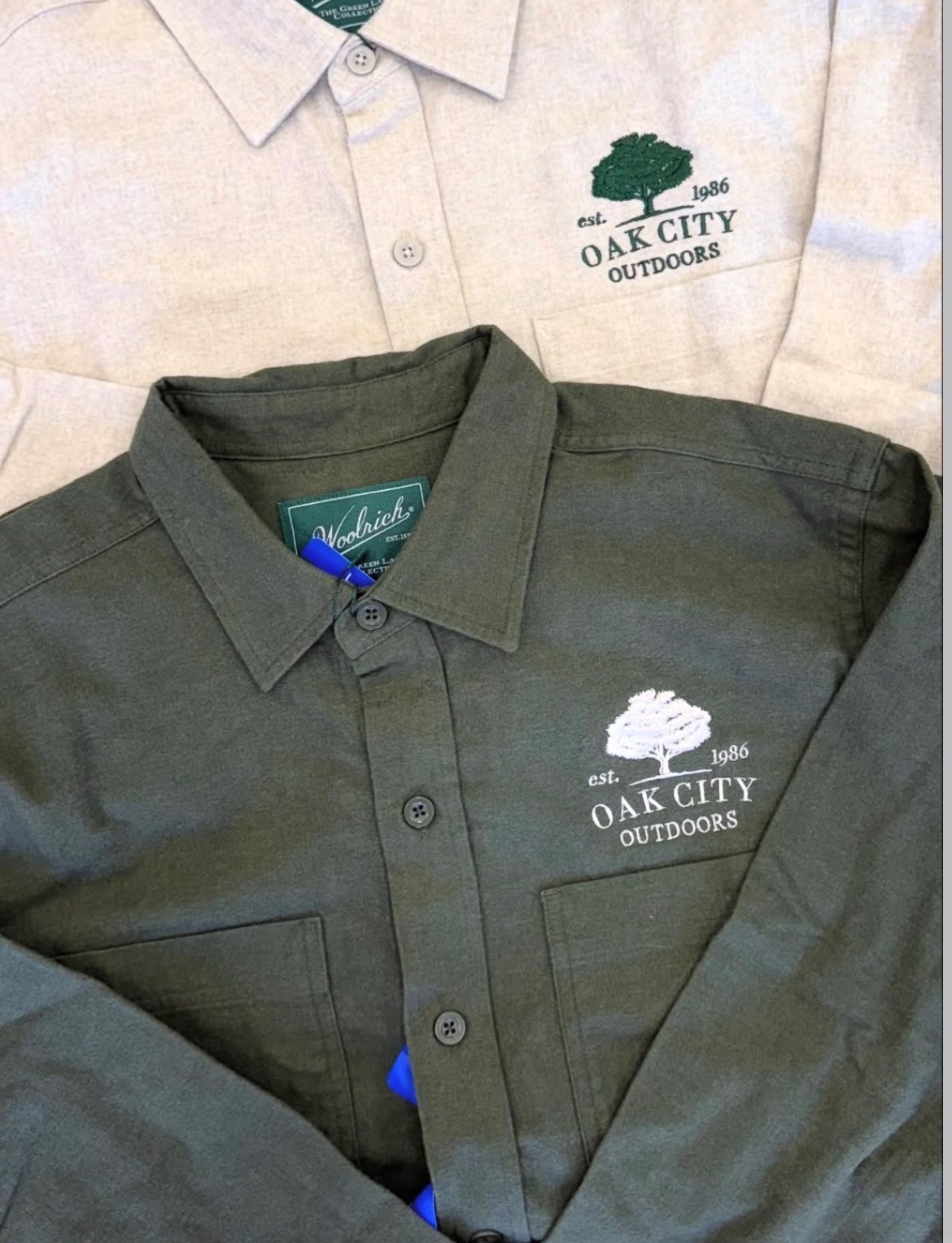 Two collared shirts with Oak City Outdoors logo, one white and one dark green, displayed side by side.