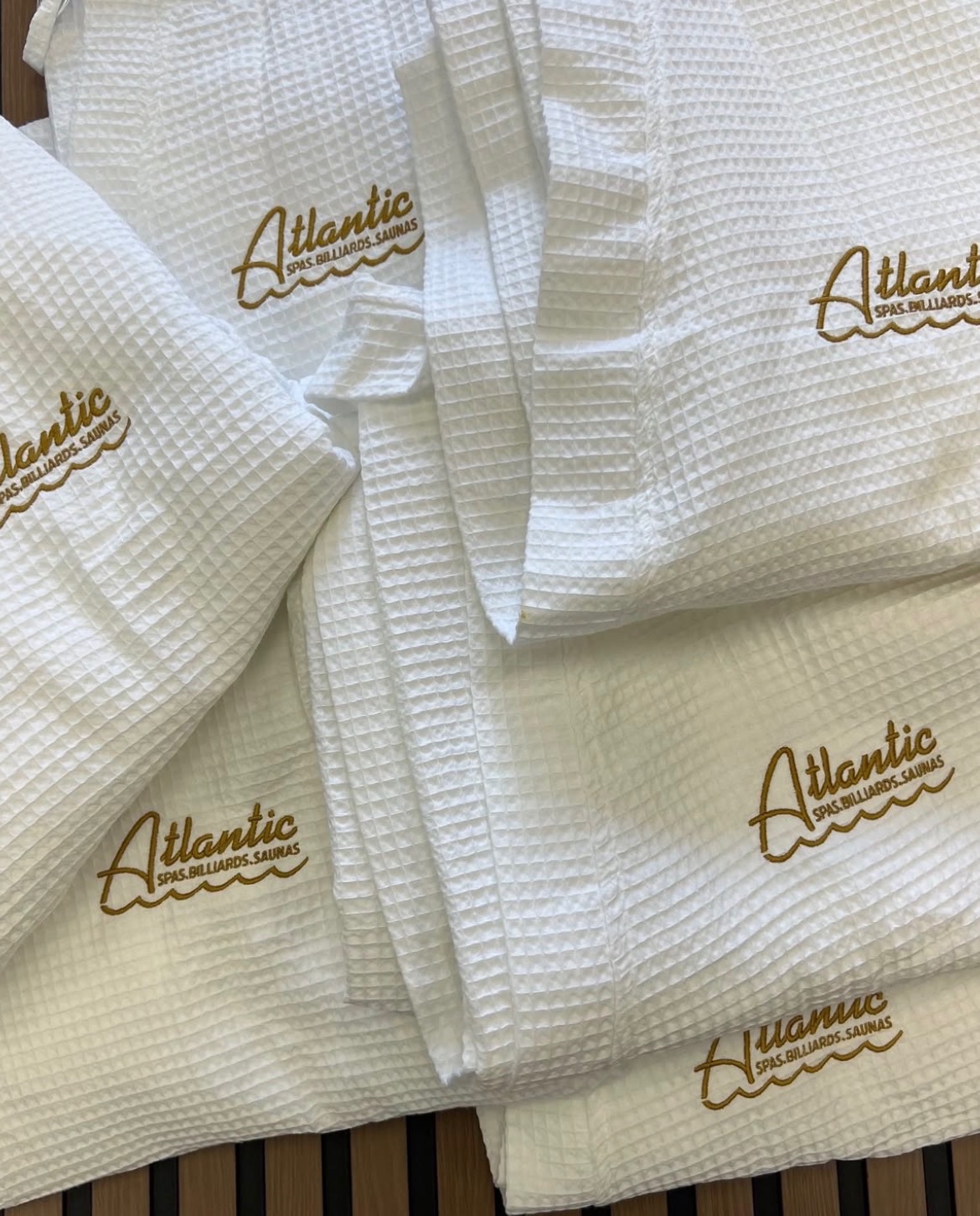 White textured fabric with gold embroidered 'Atlantic' logo, folded neatly, on a wooden surface.