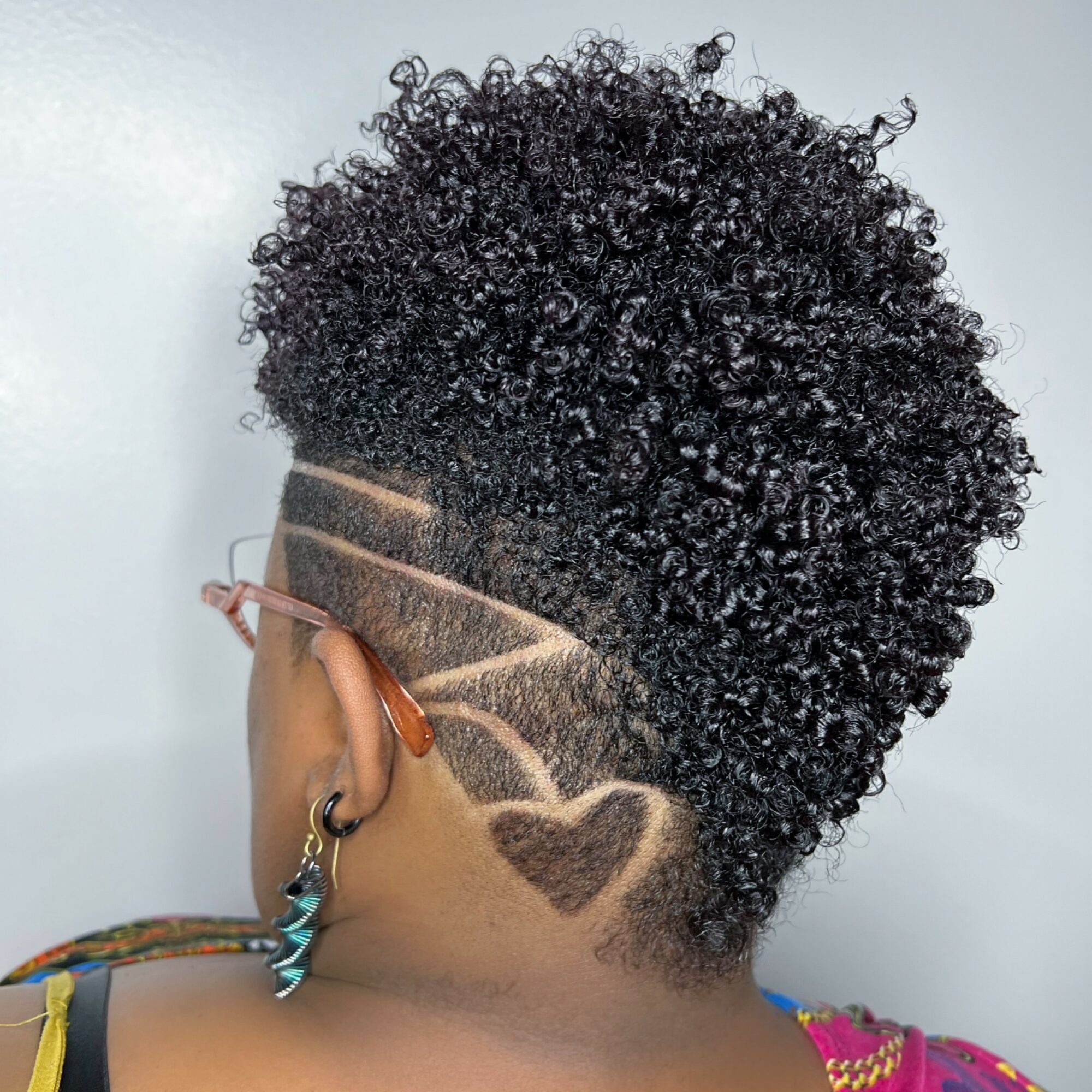 Back view of a person with a curly mohawk hairstyle and shaved design on the side of the head.