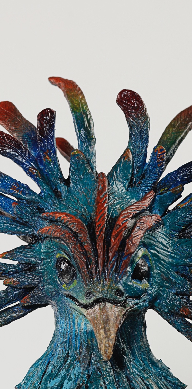 Colorful, feathered creature with a beak and large eyes, resembling a mythical or fantasy bird, against a plain background.