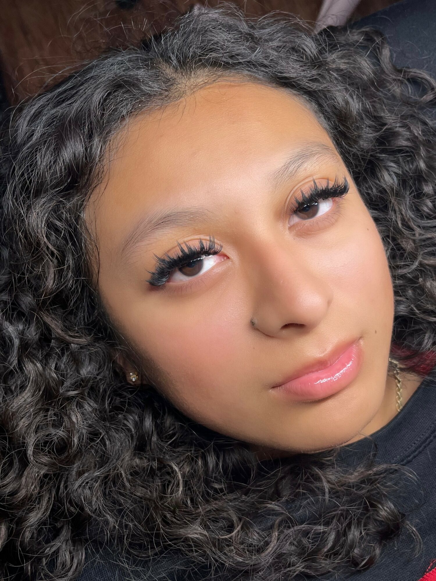 Close-up of a young woman with curly hair and makeup, looking at the camera.