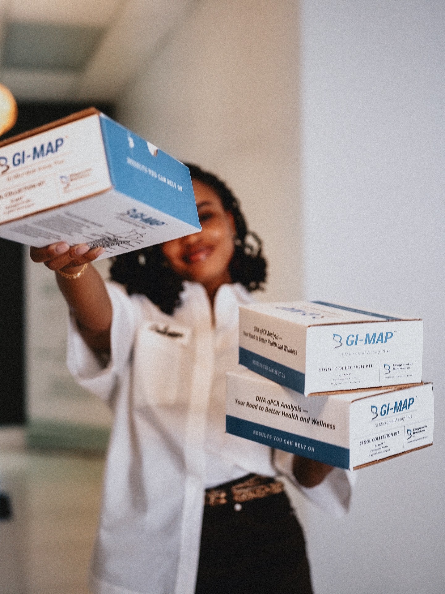 Person holding two boxes of GI-MAP test kits, smiling, in an indoor setting.