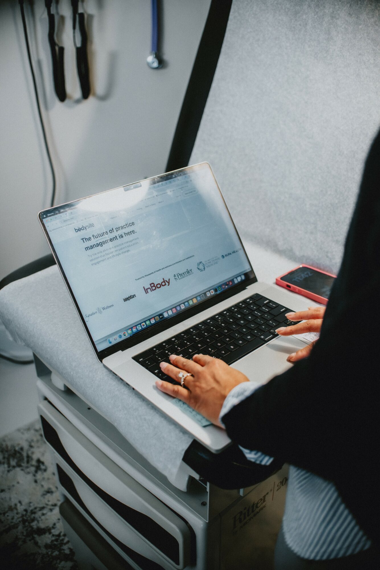 Person typing on a laptop with a webpage open, placed on a gray surface, with a smartphone nearby.