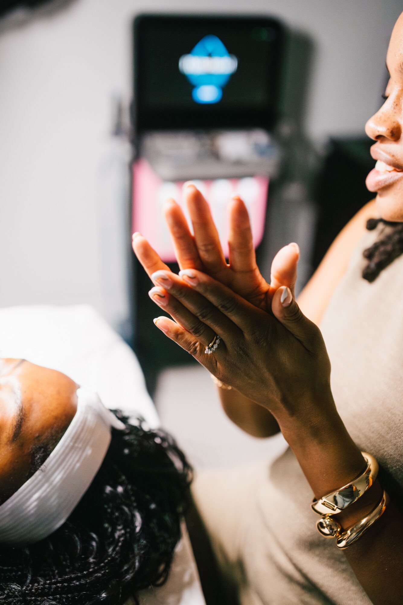 Close-up of a woman clapping her hands in a medical setting with a patient lying down, medical equipment in background.