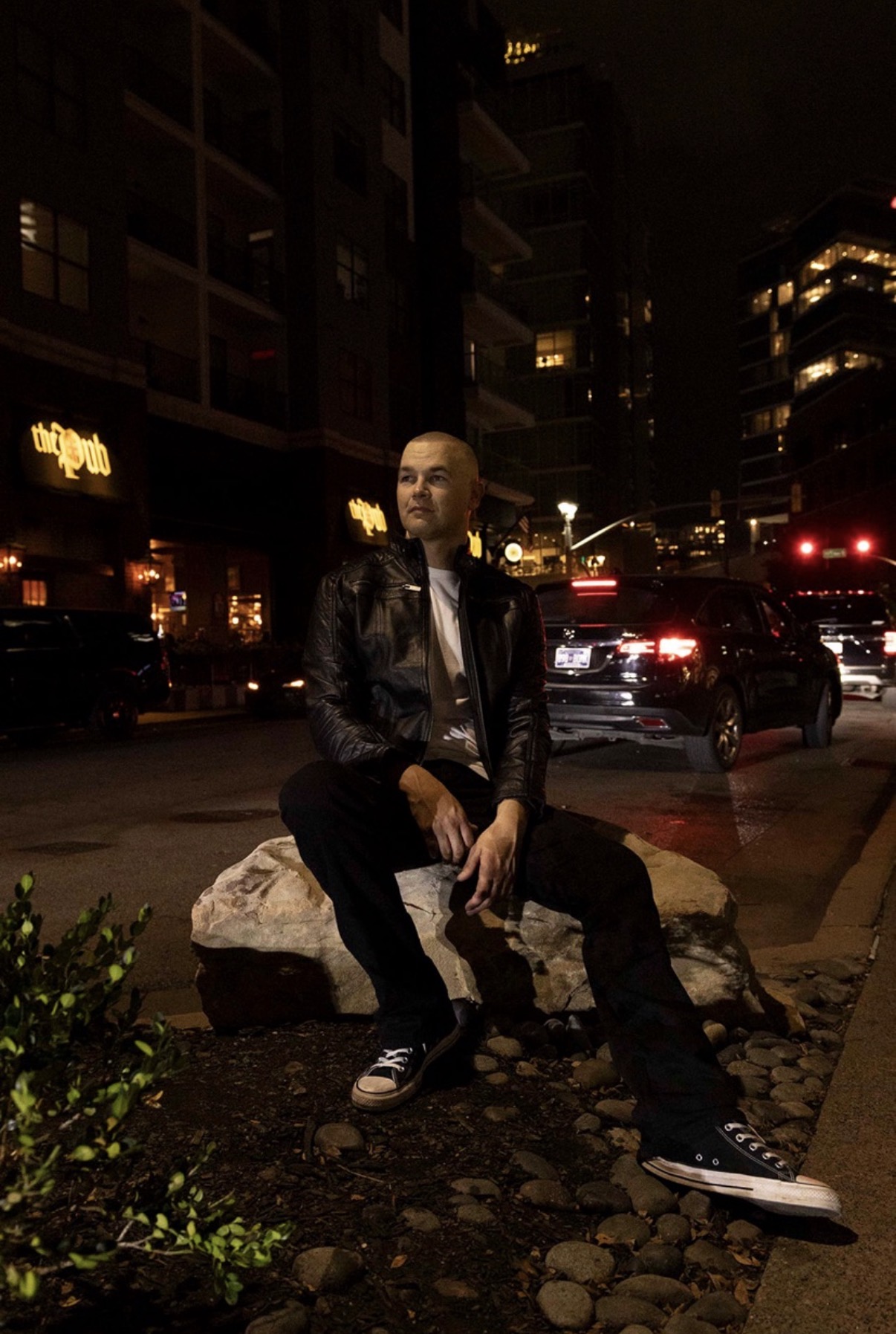 Person sitting on a rock at night in an urban area with buildings and cars around.