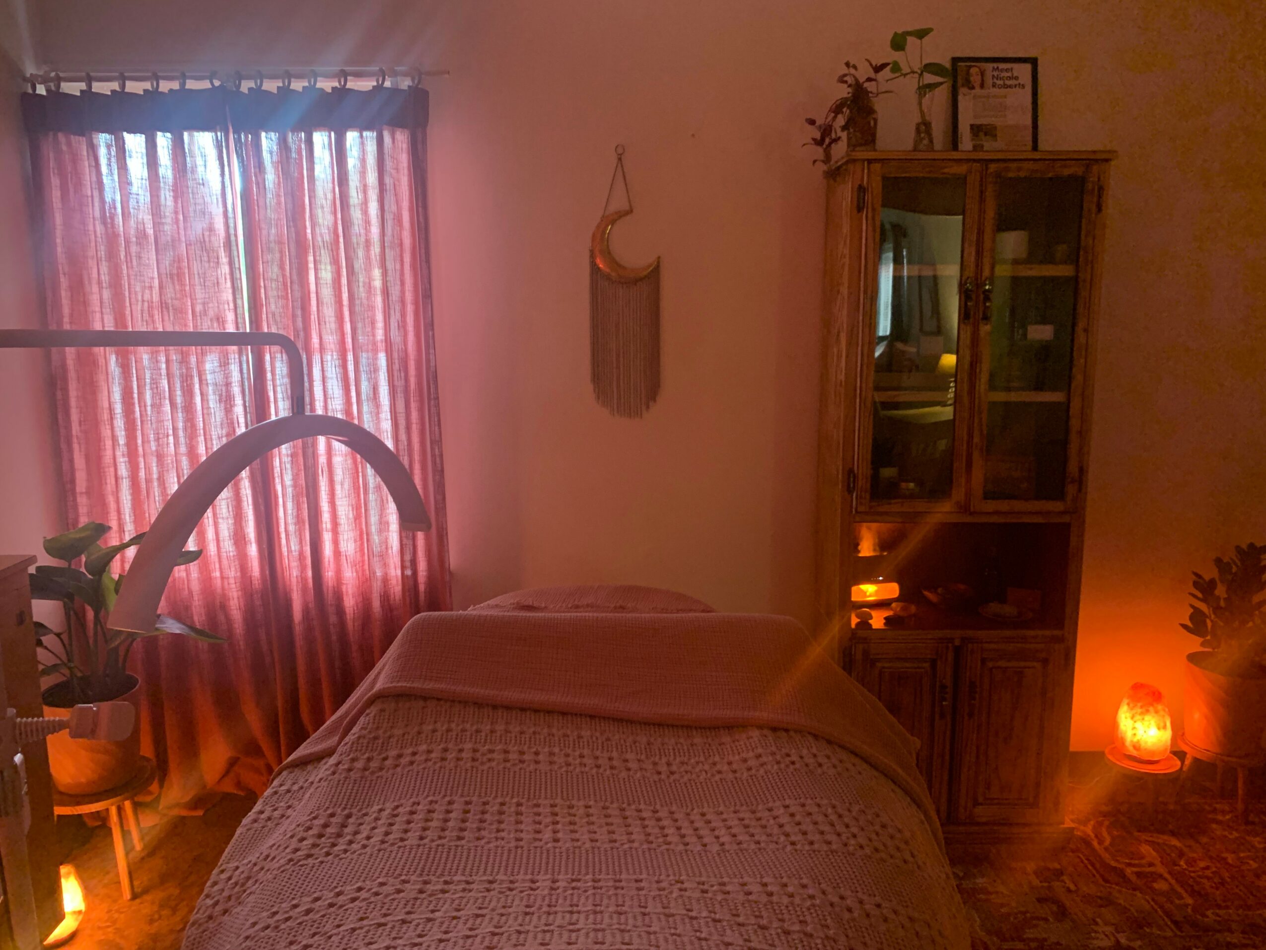 A bedroom with a bed, window with curtains, a cabinet, and warm lighting, including a Himalayan salt lamp.