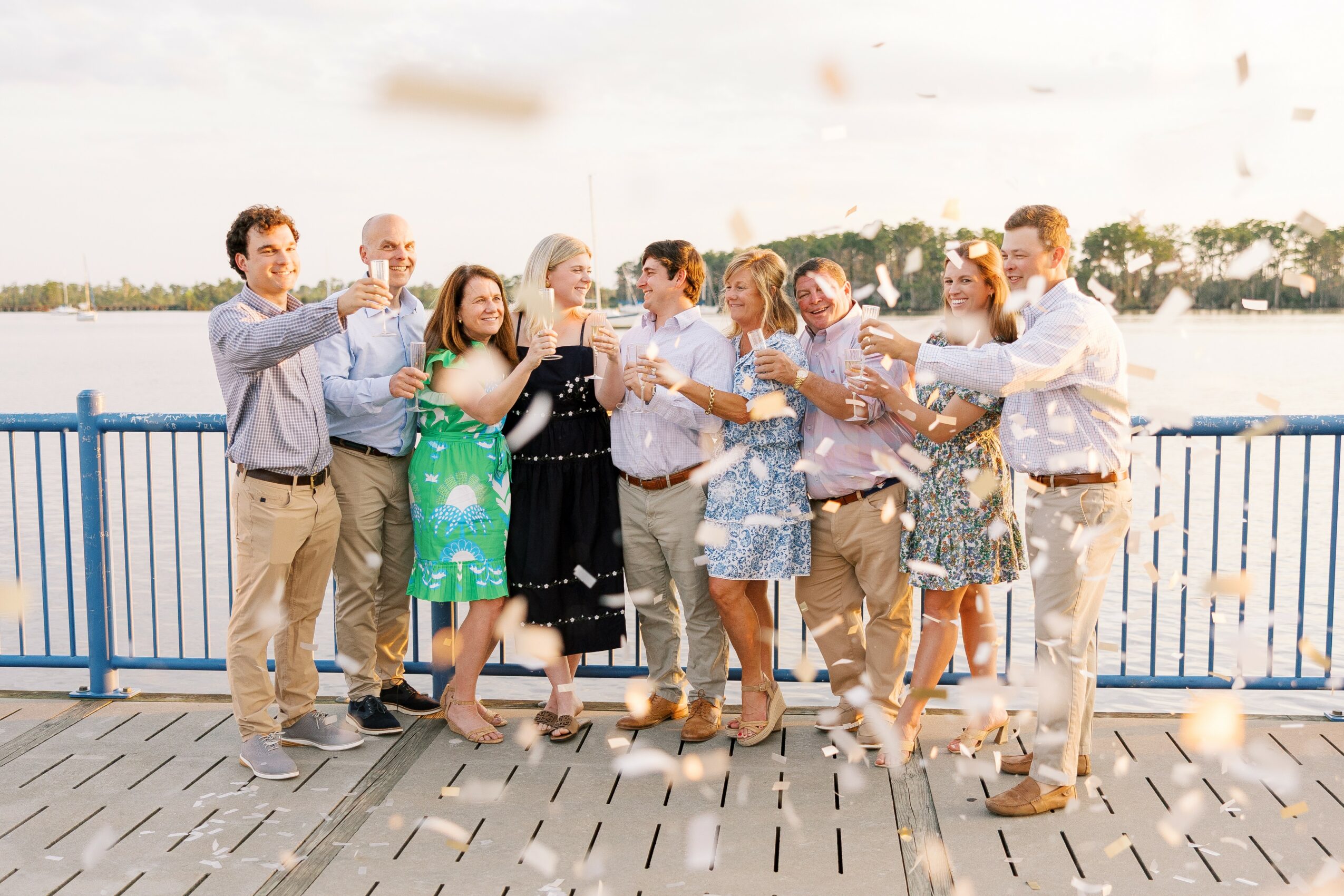 Group of people celebrating on a bridge near water, throwing confetti, smiling, and enjoying the moment.