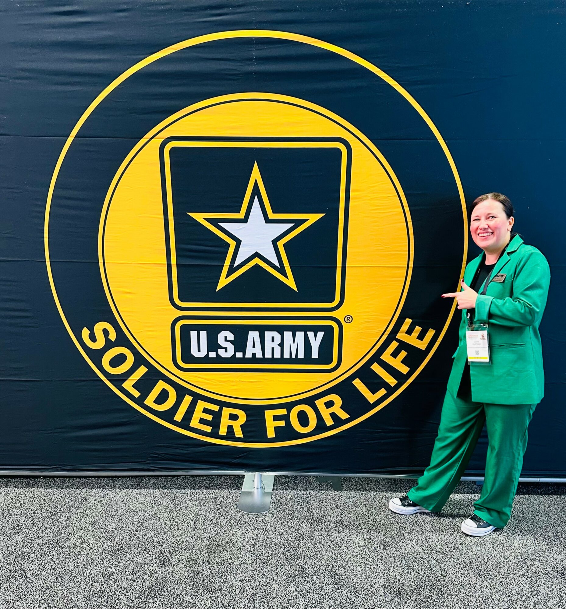 Person in green suit standing next to a U.S. Army logo with the text 'Soldier for Life'.