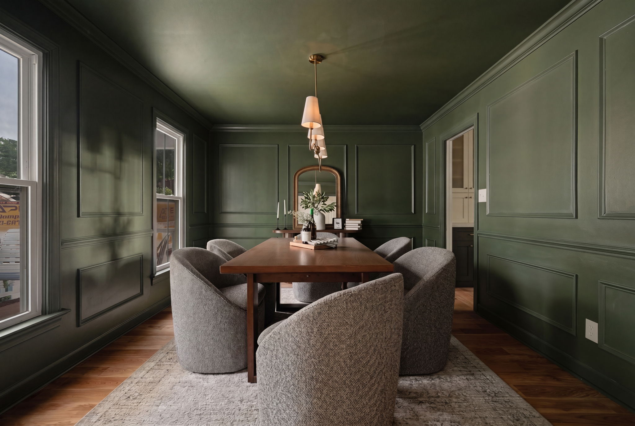 Dining room with green walls, wooden table, six gray chairs, chandelier, windows, and a rug.