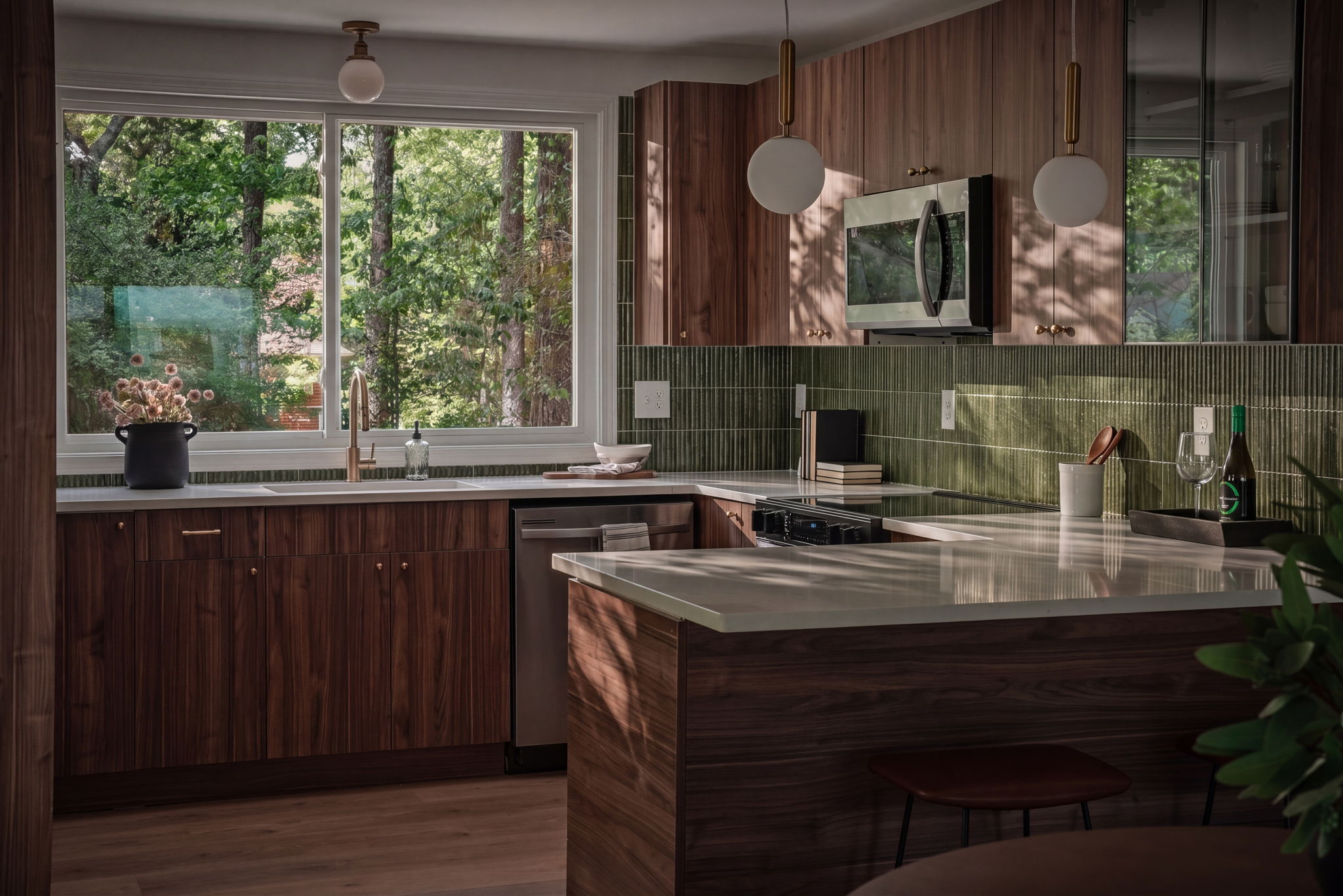 Kitchen with wooden cabinets, green tiled backsplash, window showing trees, and a white countertop with various items.
