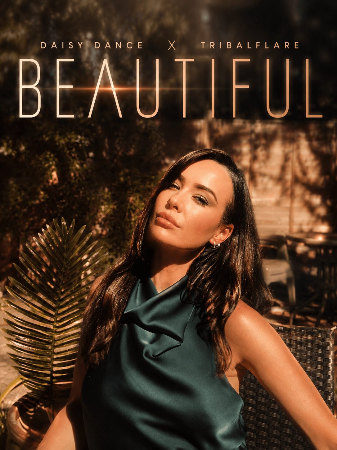 A woman with long dark hair poses outdoors with sunlight, plants, and a wicker chair in the background.