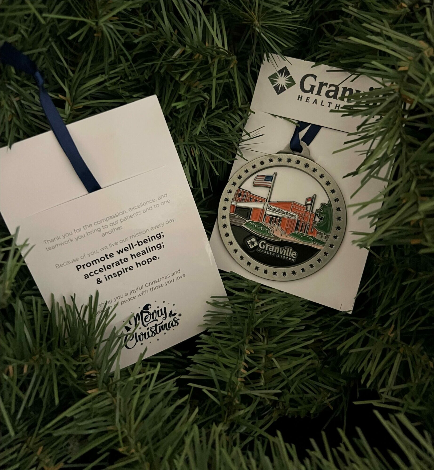 Two cards placed among green pine branches, one showing a circular logo with a building and the other with text and a ribbon.