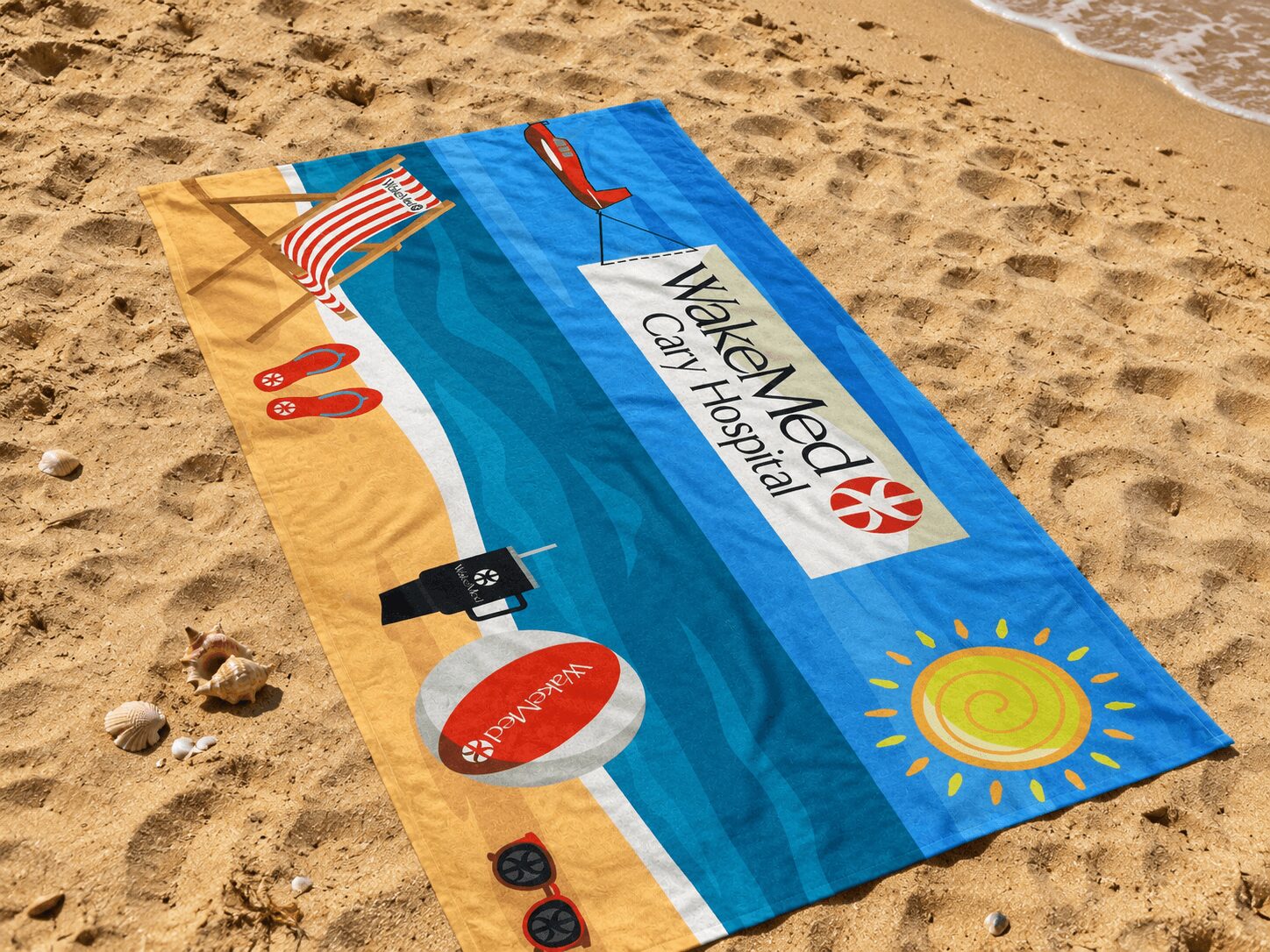 Beach towel with a sign reading 'WakeMed Coastal Hospital' on sandy beach, with seashells and ocean waves nearby.