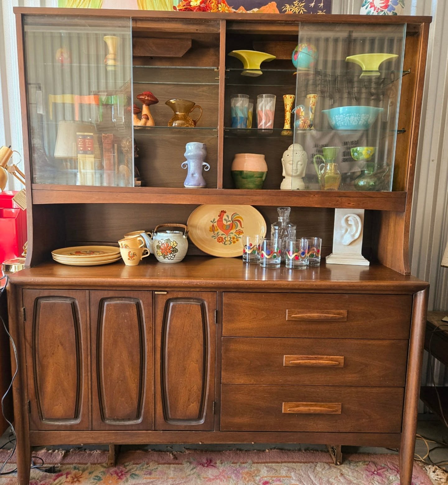 Wooden cabinet with glass doors on top, displaying decorative items, and drawers and cabinets below, in a room setting.