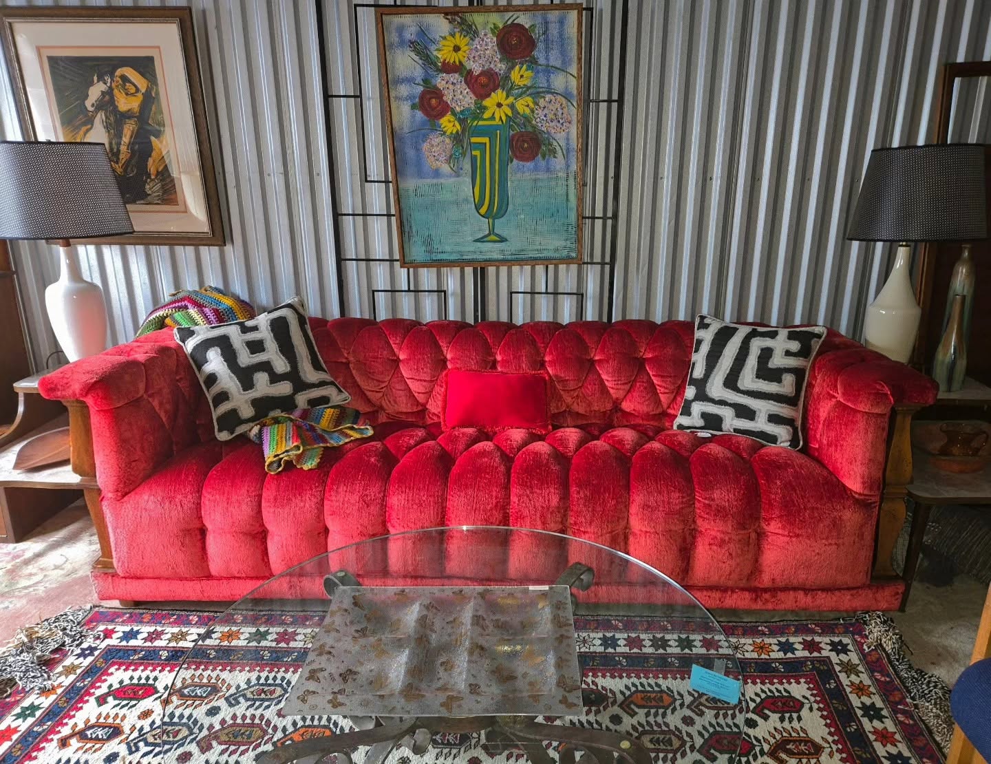 Red velvet sofa with black and white patterned pillows, in a room with artwork and lamps, and a glass coffee table.