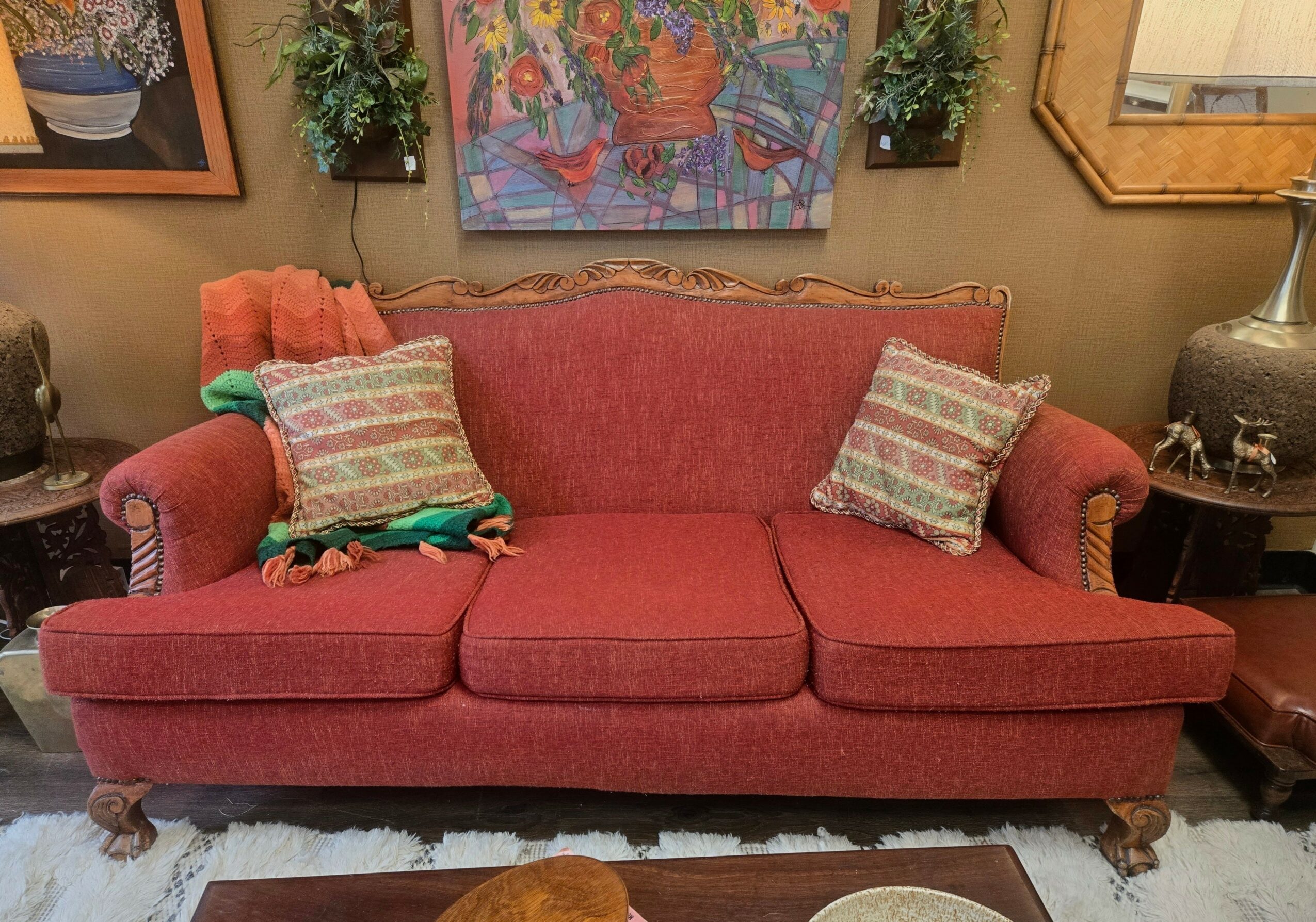 Red sofa with two patterned pillows, surrounded by artwork and plants on the wall, and side tables with lamps.