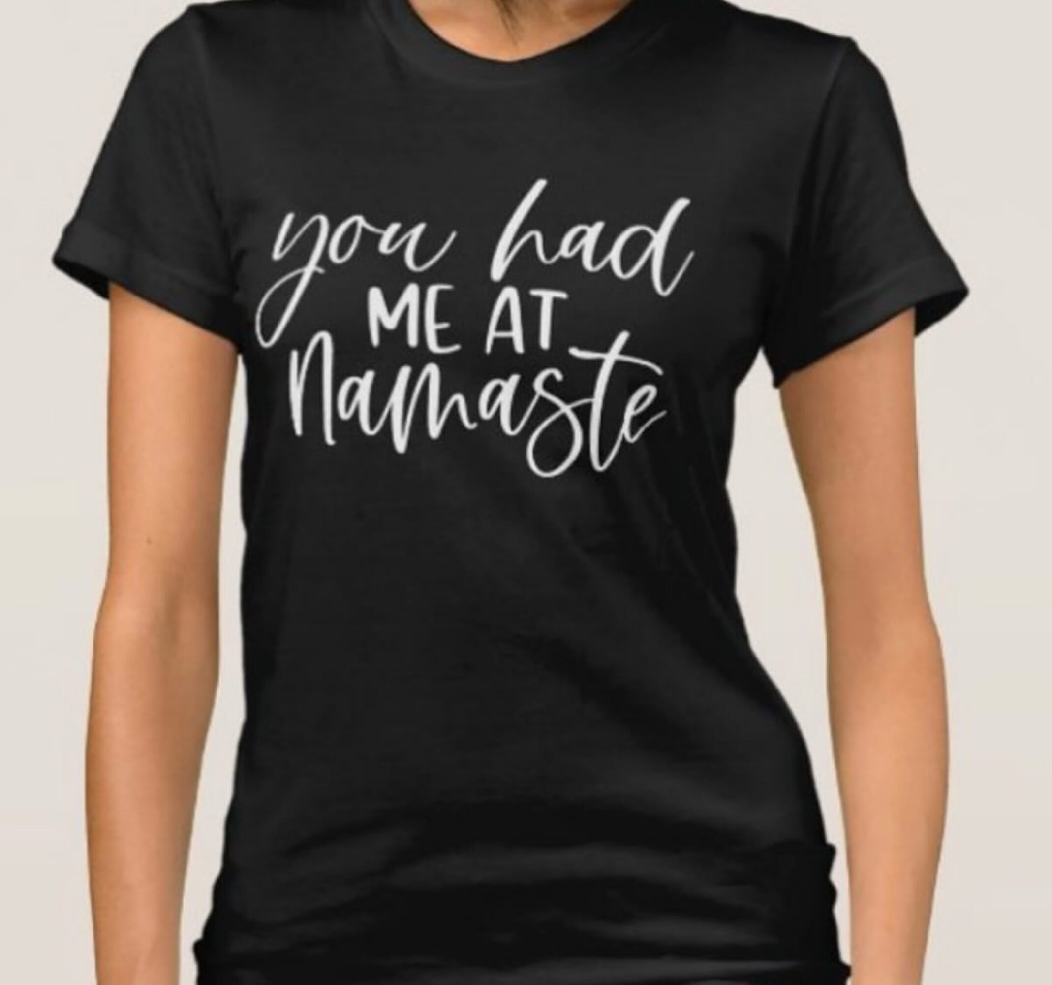 Black T-shirt with white text reading 'you had me at Namaste' on a person against a plain background.