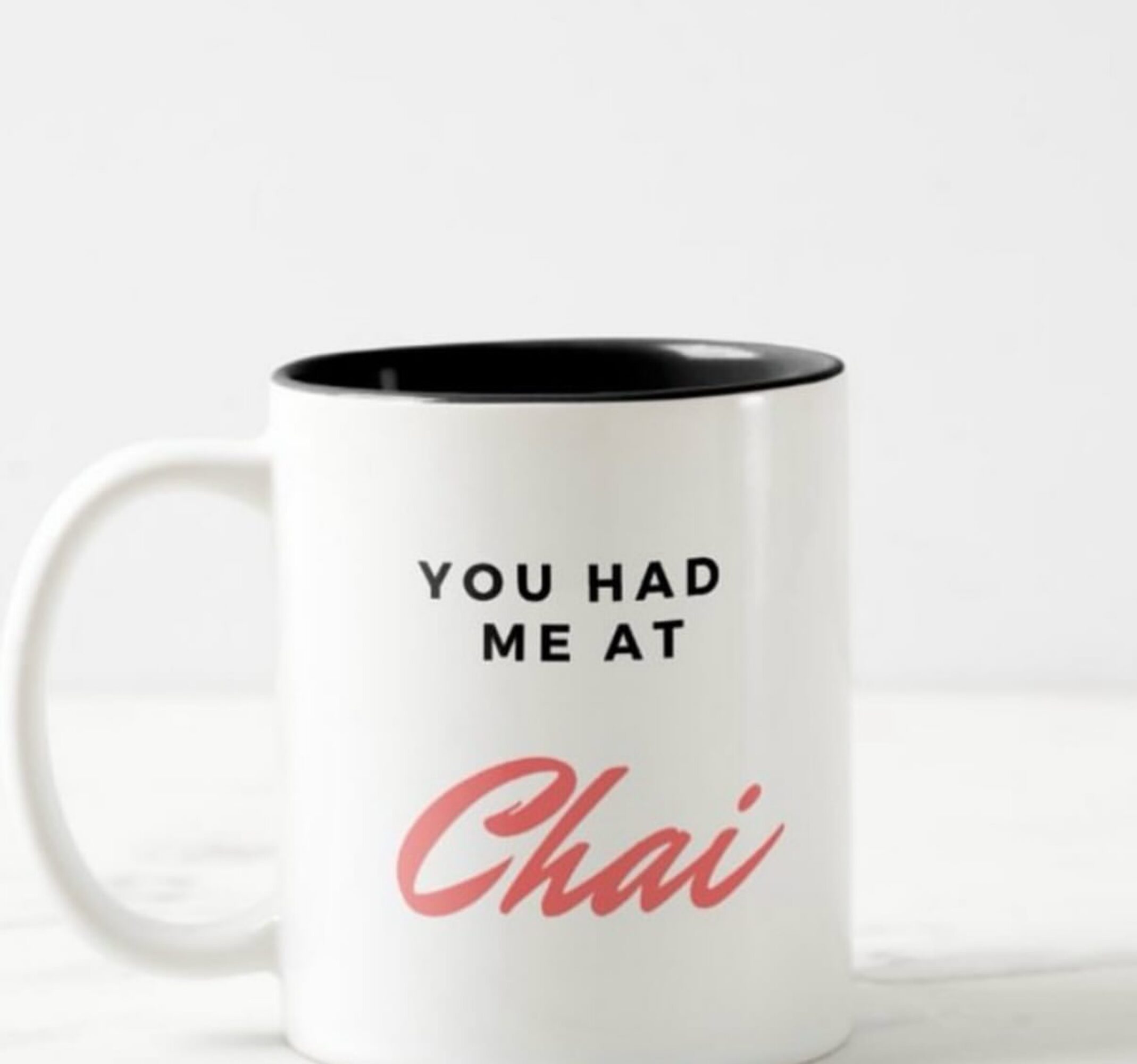 White mug with black interior and text reading 'You had me at Chai' in black and pink, on a white background.