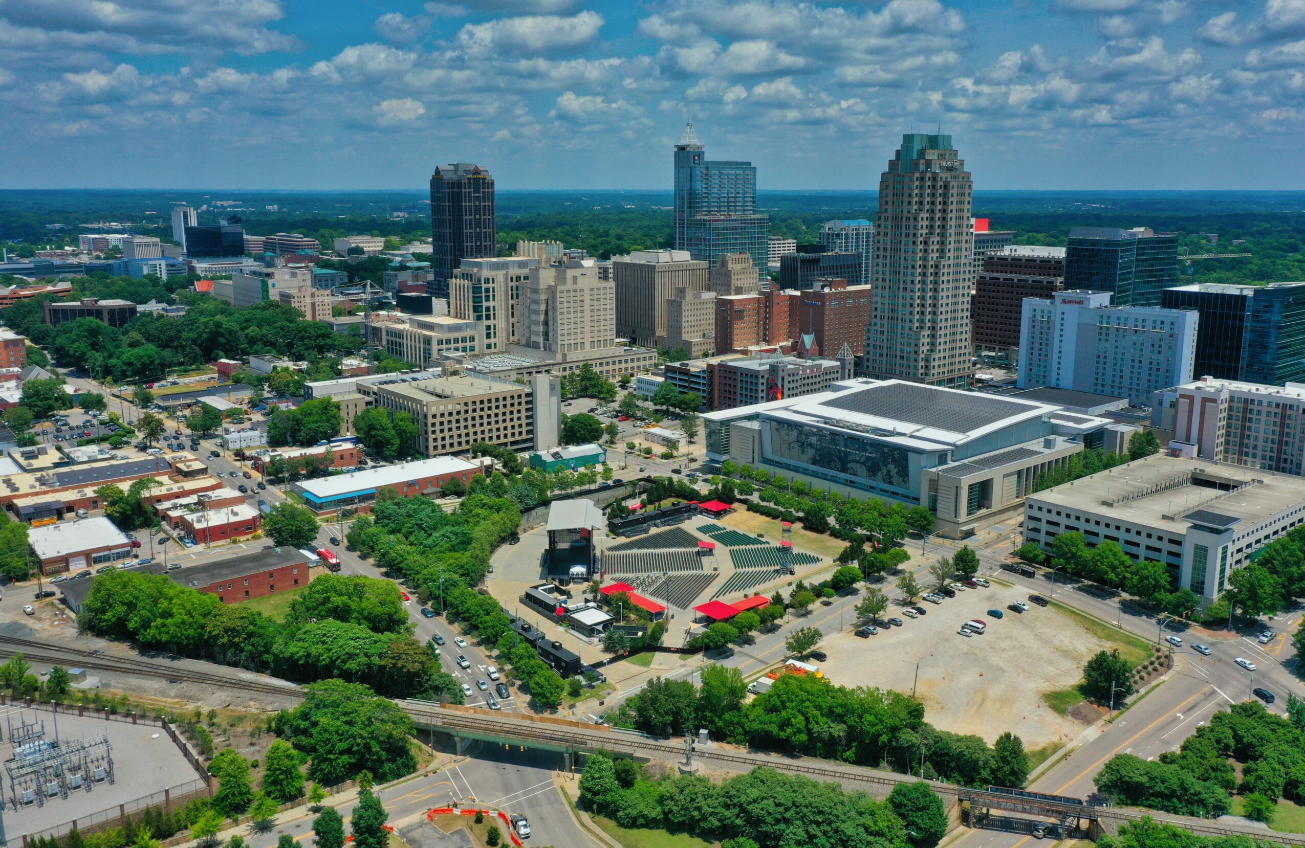 Aerial view of a city with tall buildings, green trees, and a large open area with red structures.