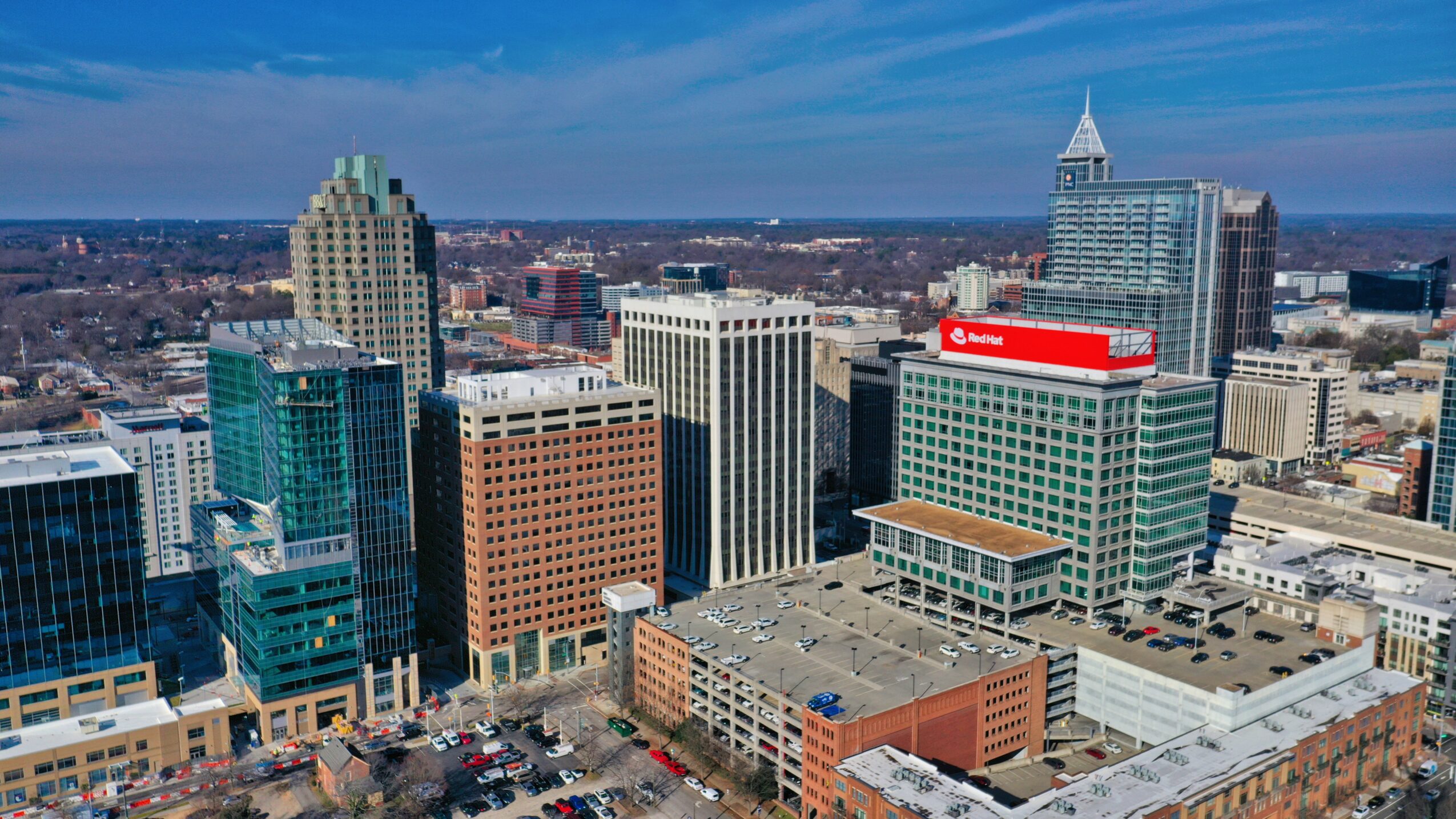 City skyline with tall buildings, including a glass skyscraper and a building with a red sign, under a blue sky.