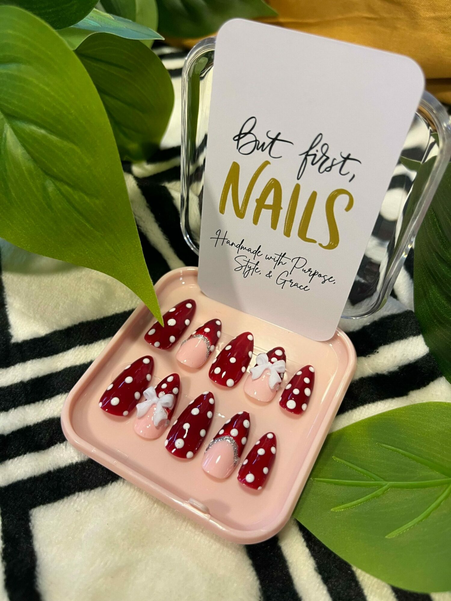 Pink case with red and white polka dot nail decals, surrounded by green leaves and black-and-white striped fabric.
