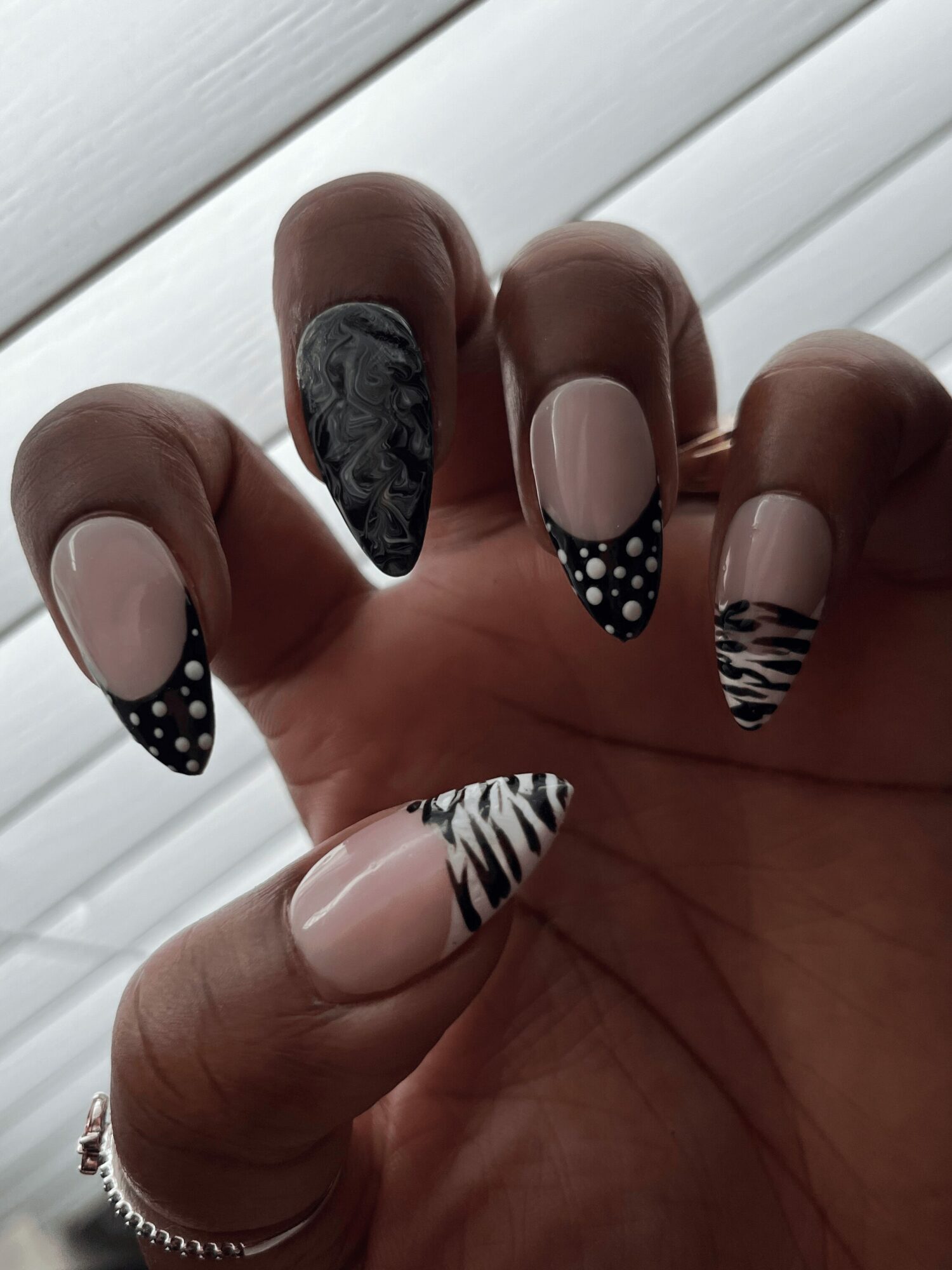 Hand with decorated nails, black and white animal print and polka dot designs, against a light background.