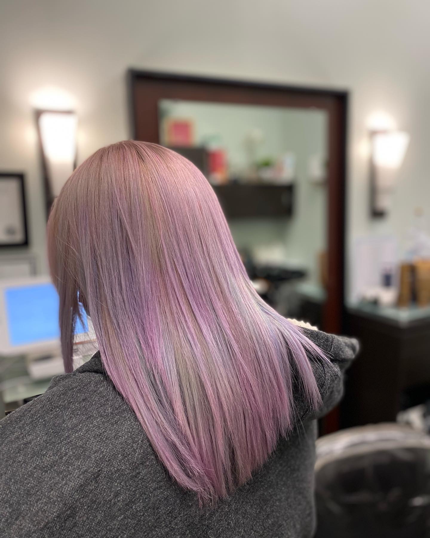 Person with pastel pink and purple hair, viewed from the back in a salon or similar setting.
