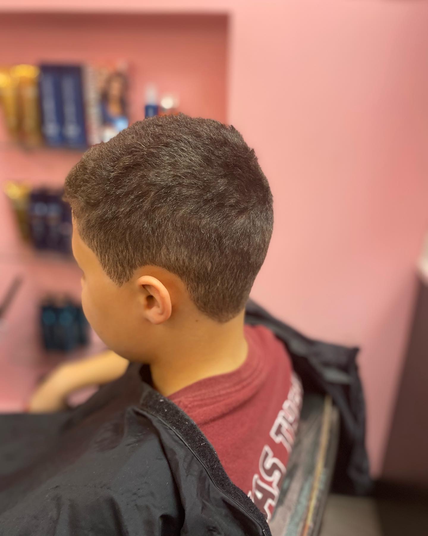 Side view of a young boy with short, dark hair, wearing a maroon shirt and black jacket, in a room with pink walls and bookshelves.