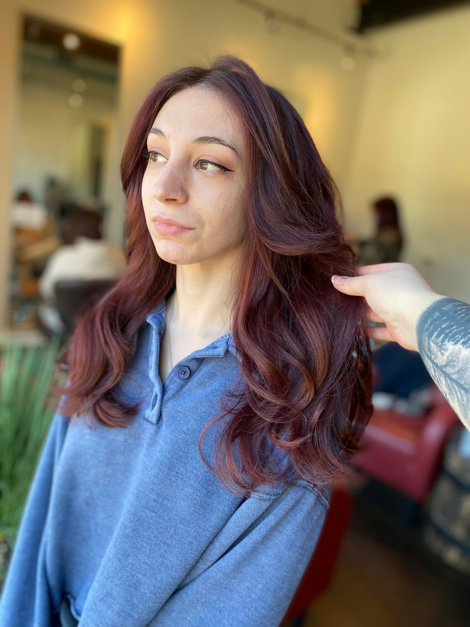 Young woman with long, wavy, reddish-brown hair looking to the side in a salon or similar setting.