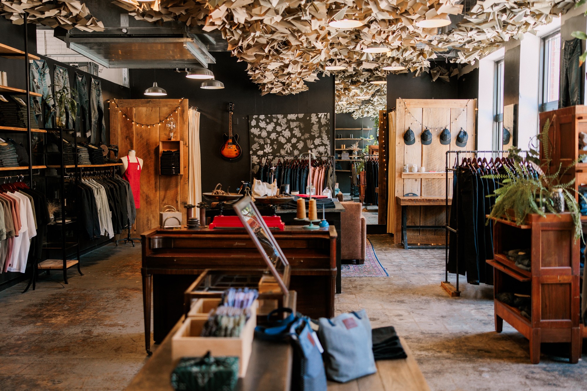 Clothing store interior with racks, shelves, and decorative ceiling elements, natural light from windows, and various clothing items displayed.