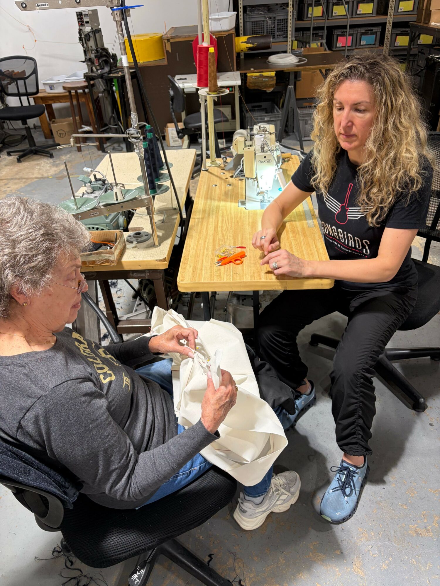 Two women seated at a table in a workshop, one with curly hair and the other with gray hair, engaged in conversation.