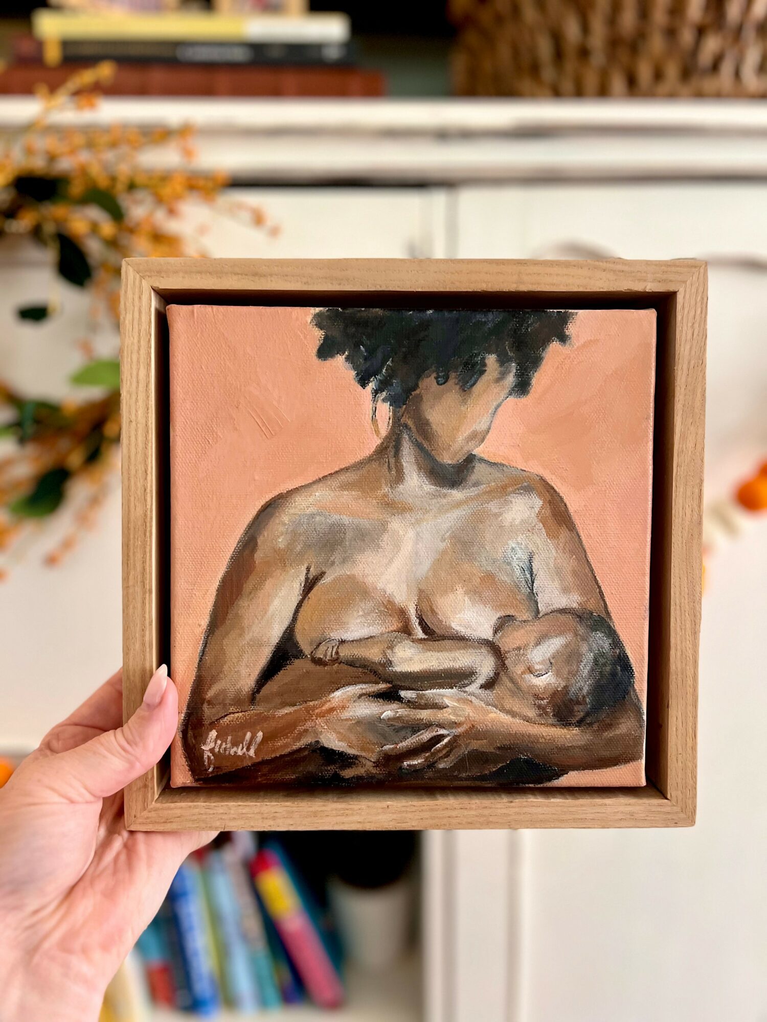 Painting of a woman with dark curly hair holding a baby, with a pink background, in a wooden frame.
