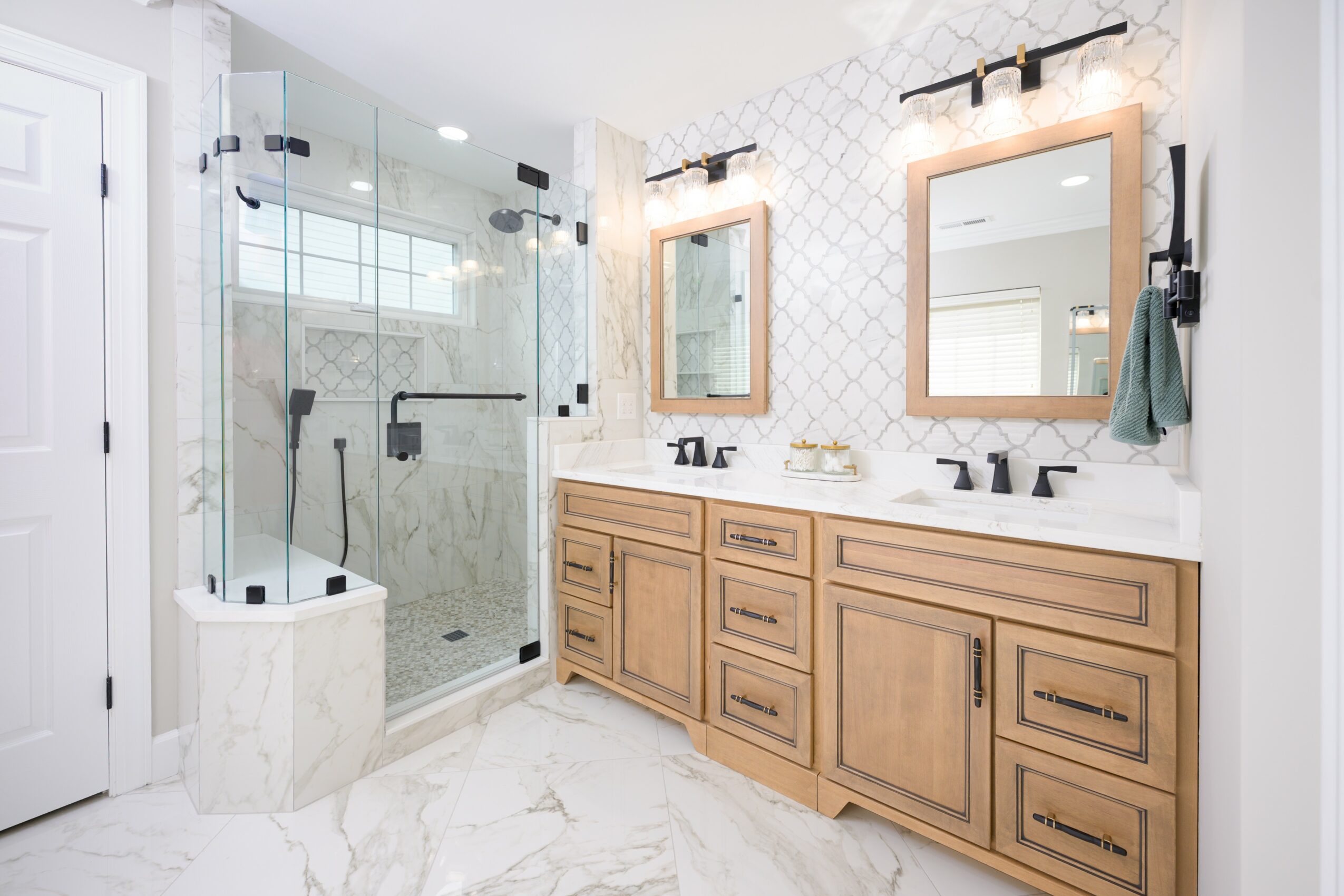 Bathroom with double vanity, two mirrors, and a glass shower enclosure with marble flooring and white walls.