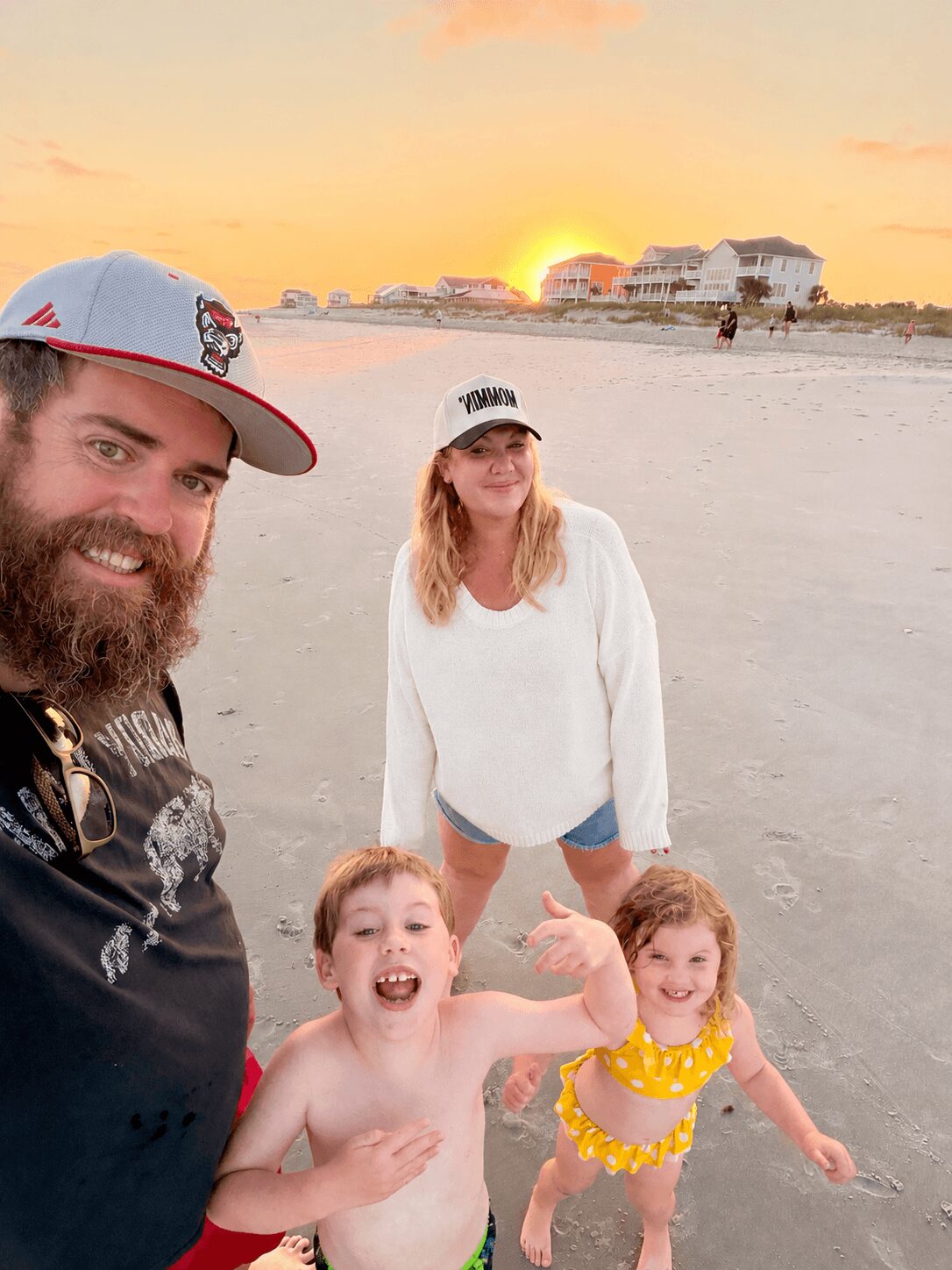 A family on the beach at sunset, with two children and two adults smiling and playing.