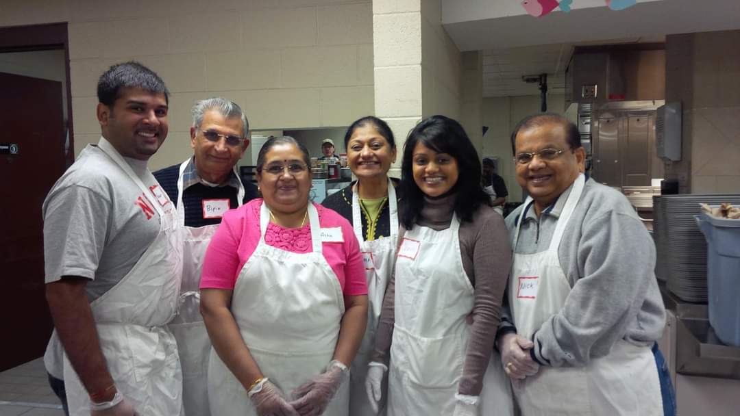 Group of six people in a kitchen, wearing aprons and smiling.