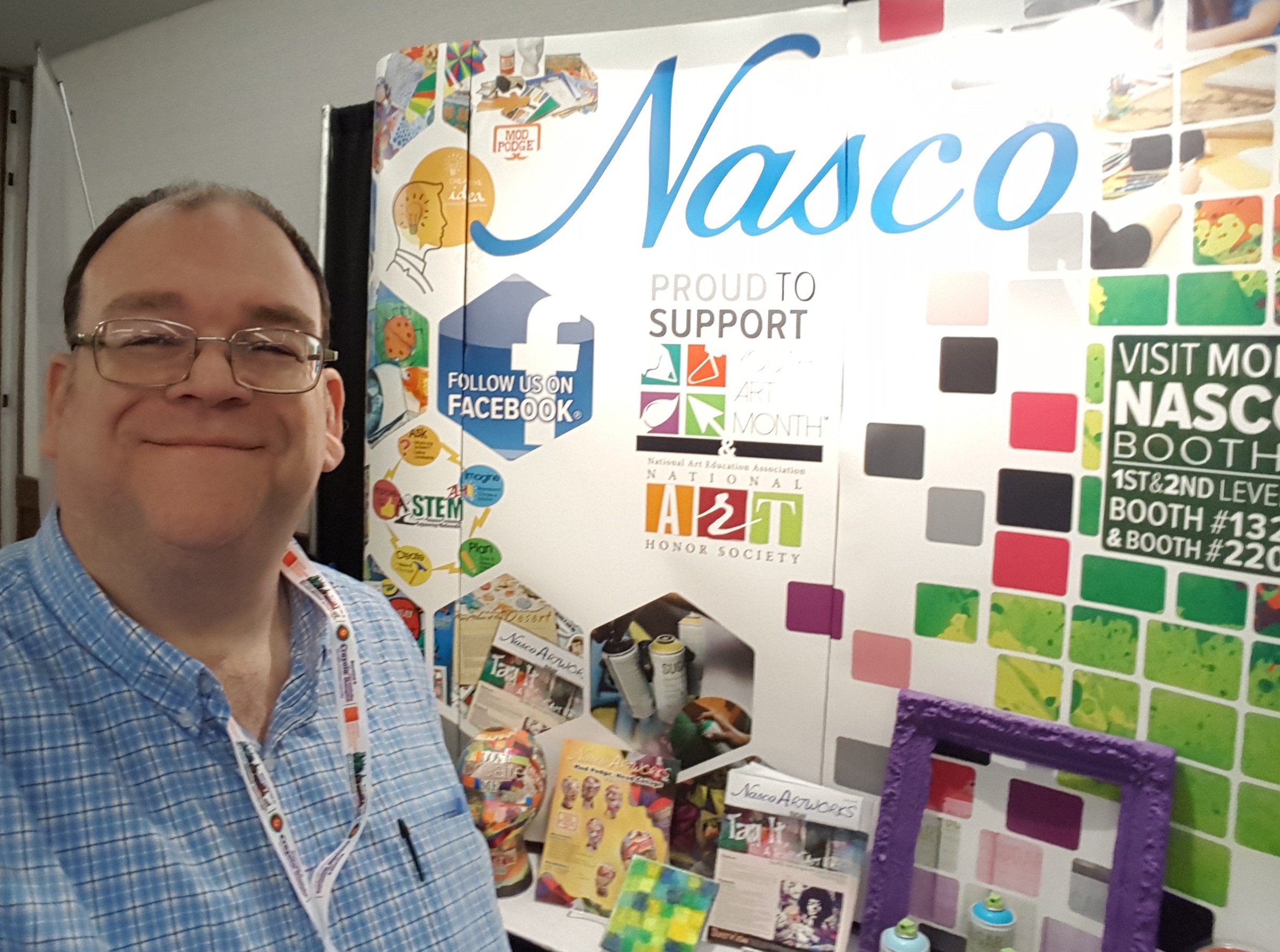 Smiling man with glasses standing next to a colorful display board with the word 'Nasco' and various images.
