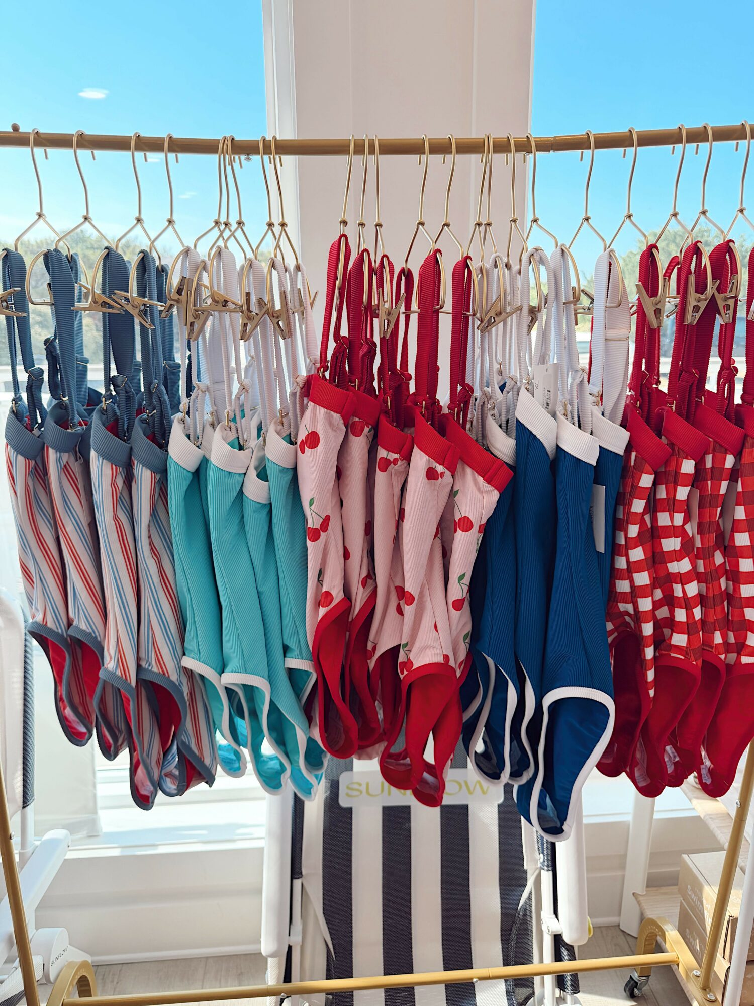 Clothes hanging on a rack, including red, white, blue, and striped garments, with a bright background and a railing.