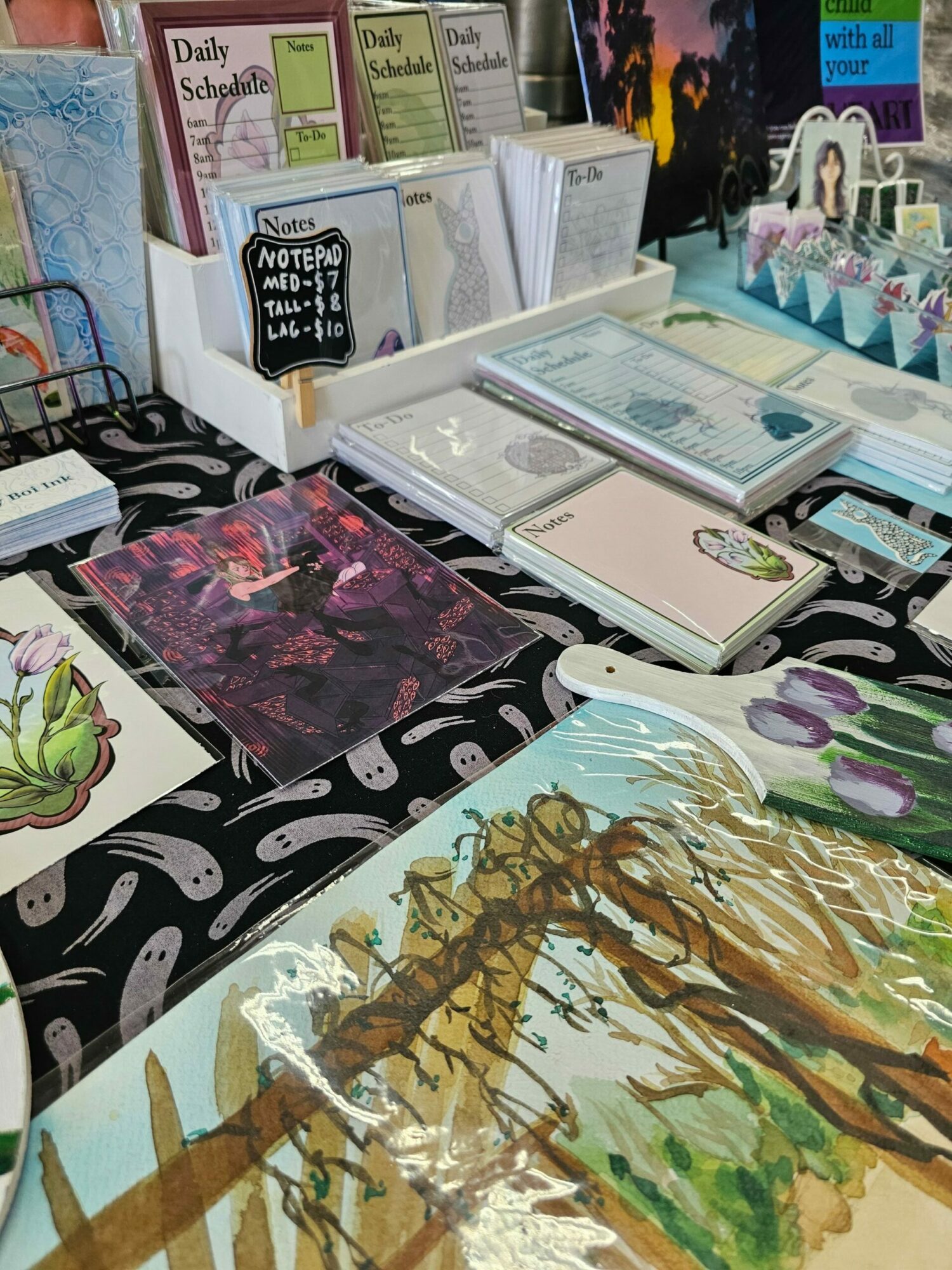 Display of various art and craft items, including paintings, framed pictures, and decorative objects on a black and white patterned surface.